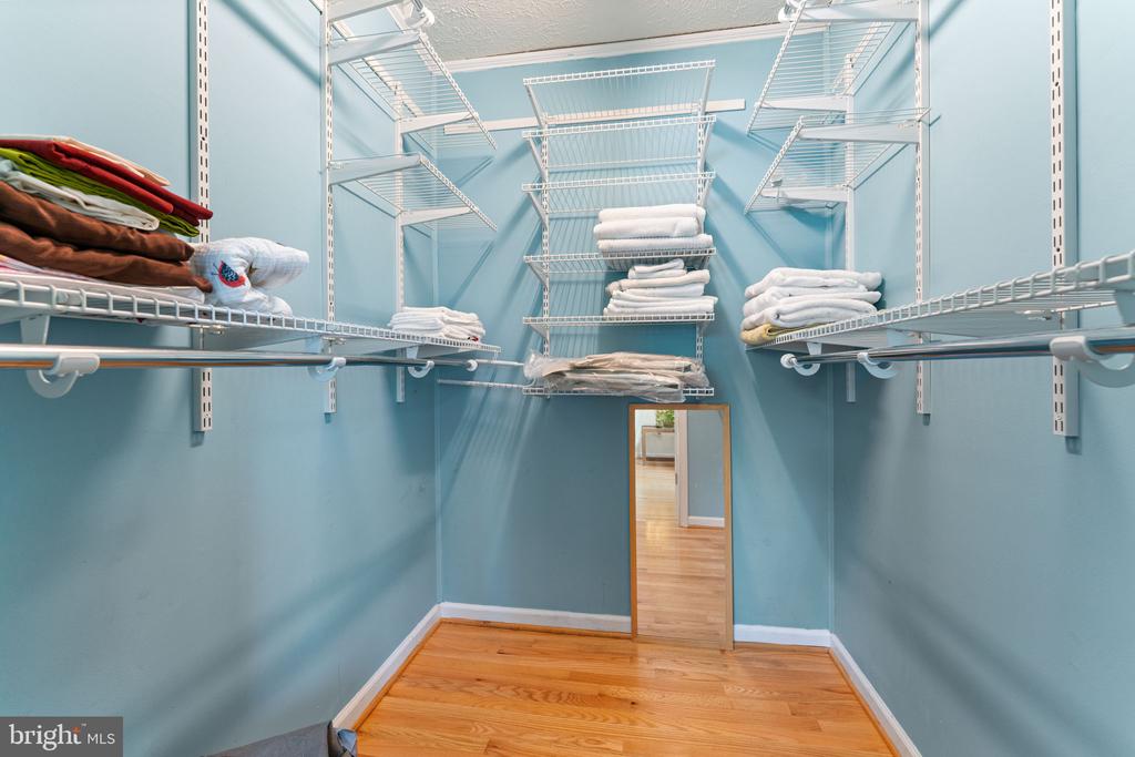 Walk-in closet with extensive white wire shelving, folded linens, blue walls, and hardwood flooring.
