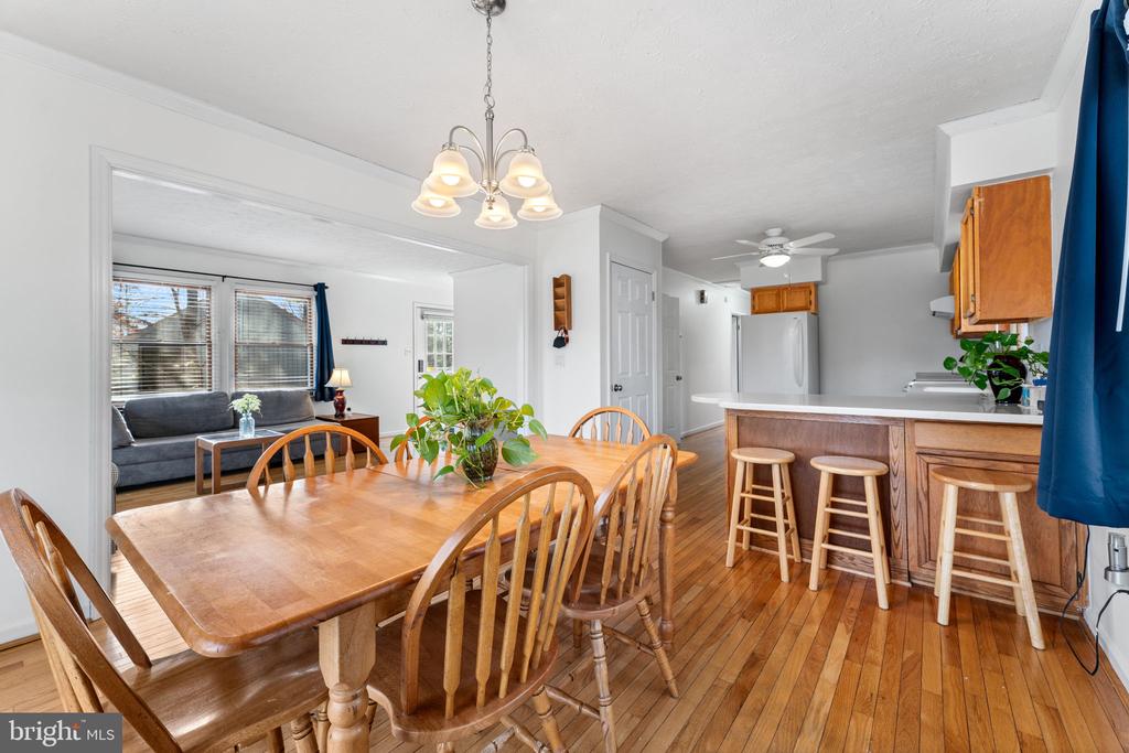 Dining area with a large wooden table, hardwood floors, and an adjoining kitchen breakfast bar.