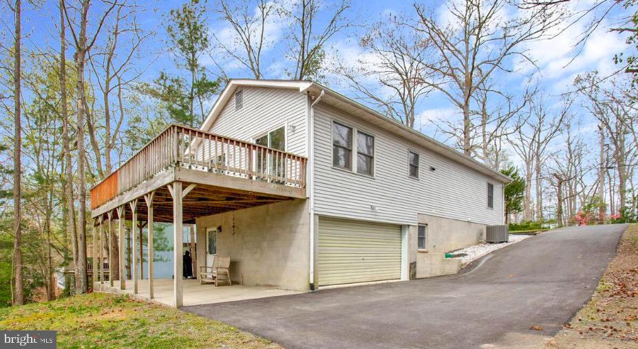 Two-story house with an elevated wooden deck, attached garage, and sloped paved driveway.