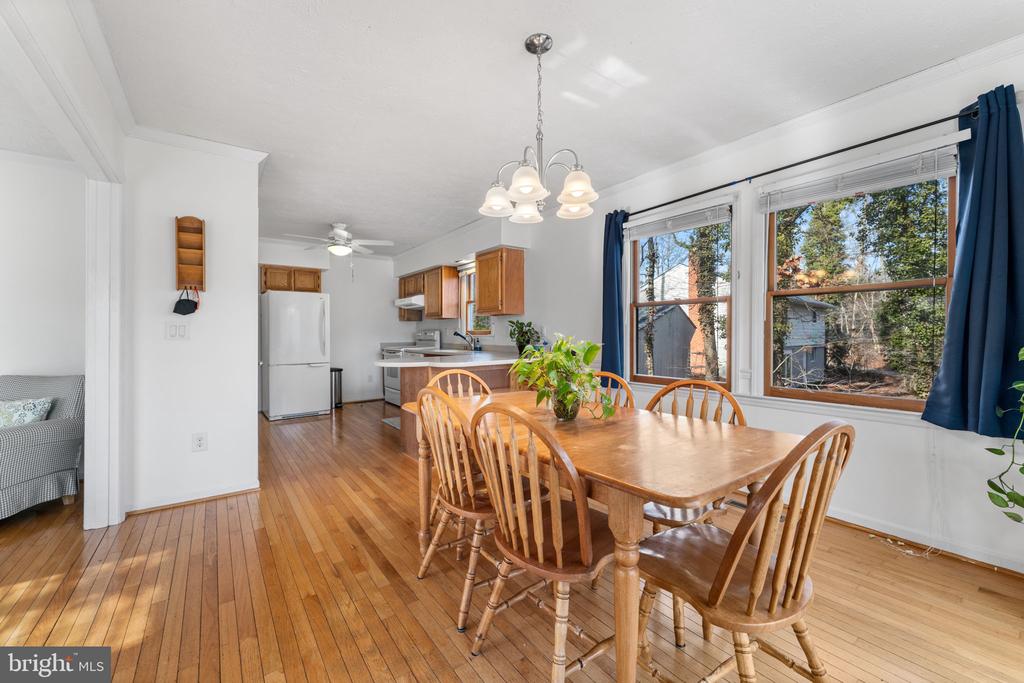 Dining area with a wooden table and chairs beside a kitchen and large curtained windows.