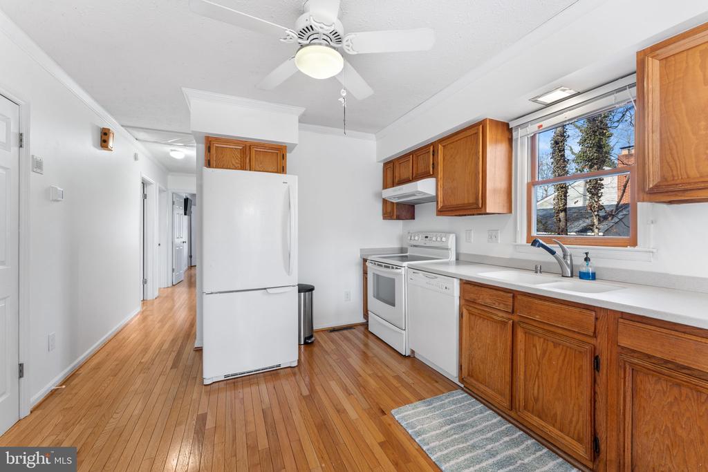 Kitchen with wood cabinets, white appliances, hardwood floors, and a window above the sink.