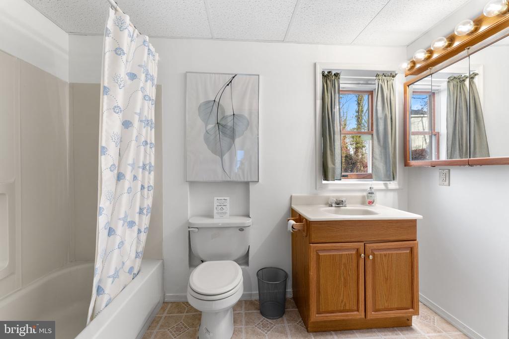 Bathroom with a blue-patterned shower curtain, wood vanity, and window above the sink.