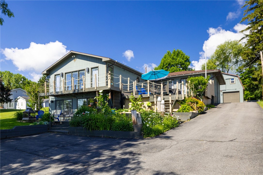 Light gray raised home with a large deck, turquoise umbrella, landscaped garden beds, and attached garage.