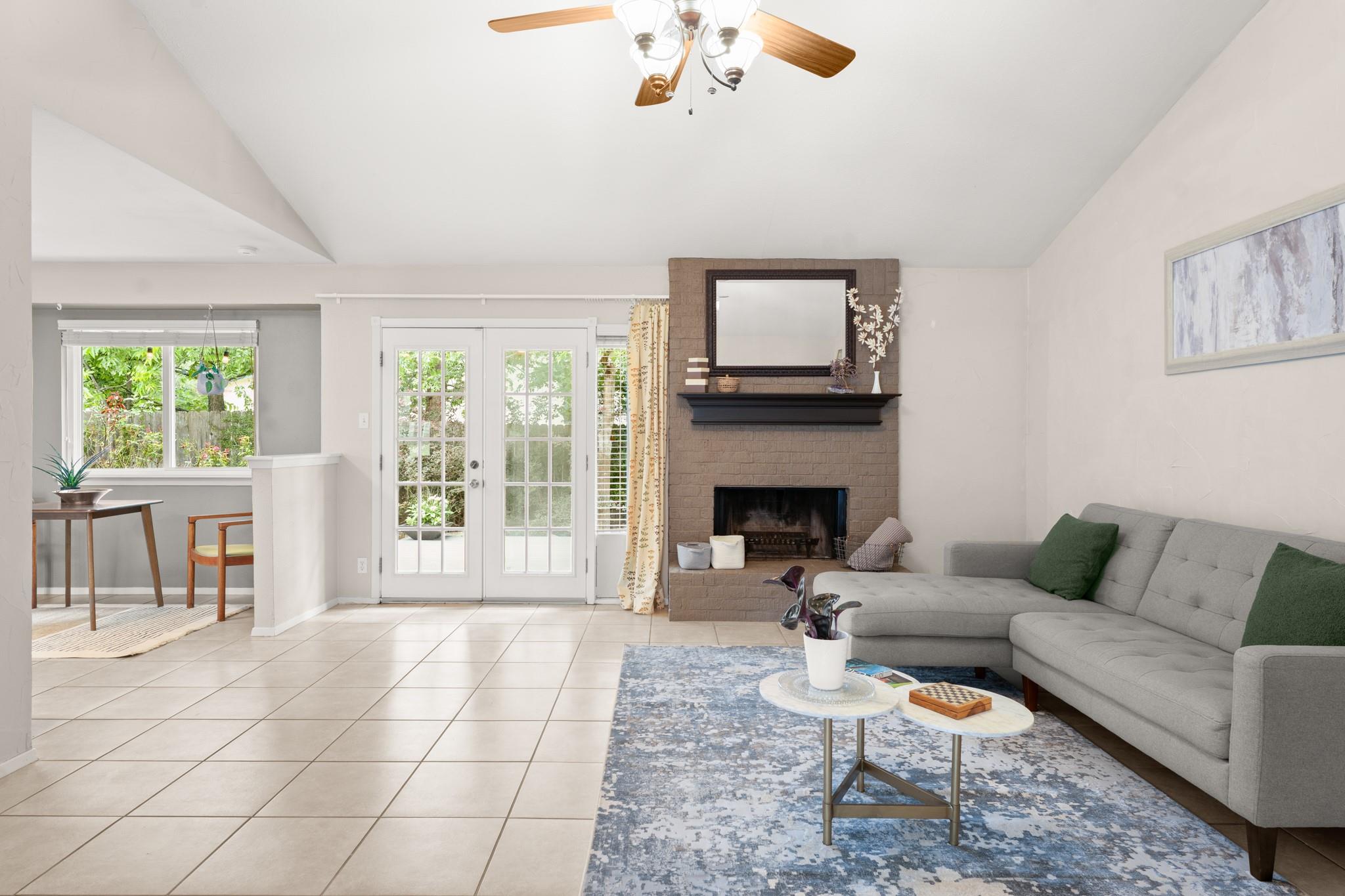 Living room with a brick fireplace, gray sectional sofa, and garden-facing French doors.