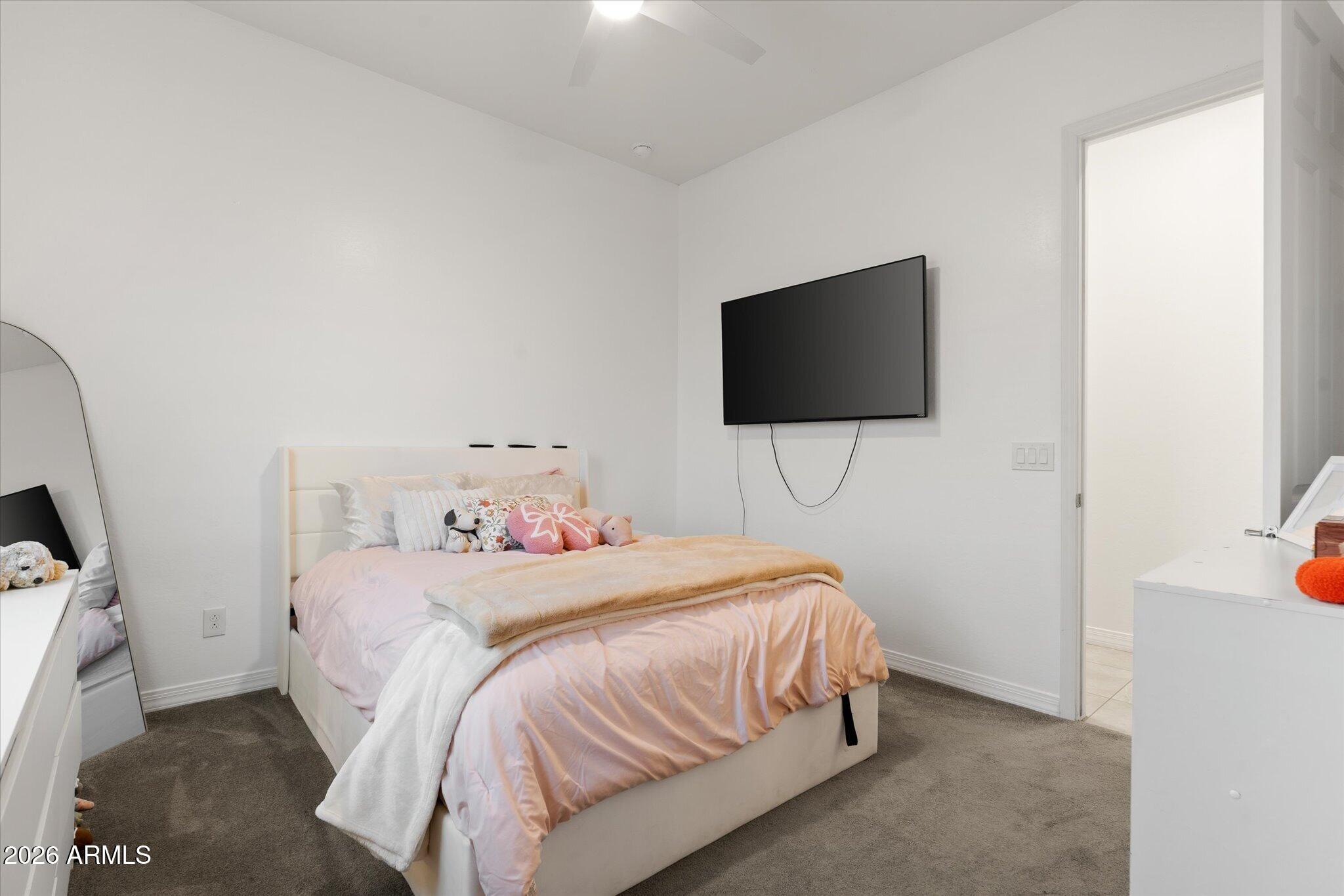 Bedroom with pale pink bedding, plush toys, and a wall-mounted television.