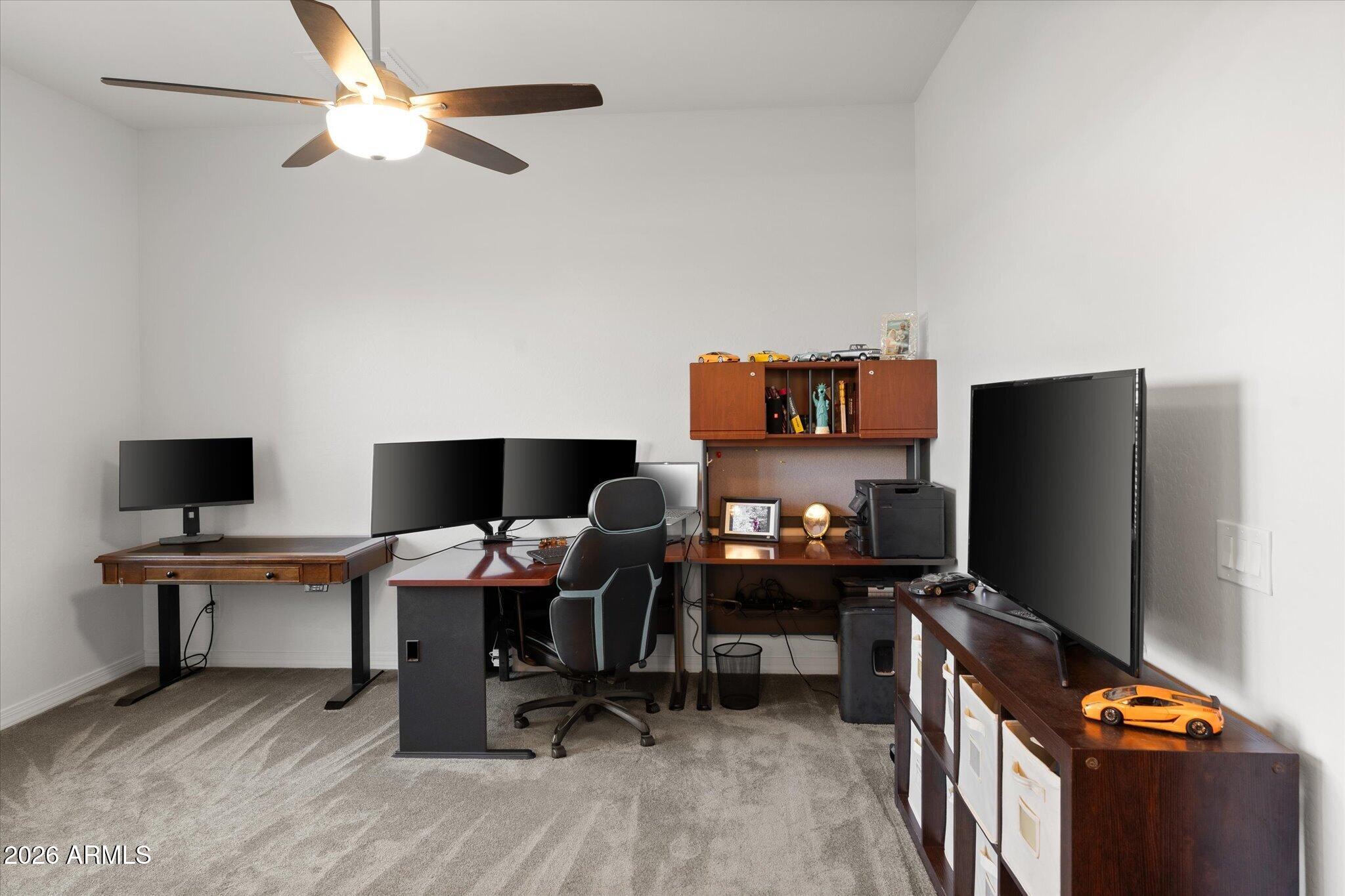 Furnished home office with multiple monitors, dark wood desks, and a large television.