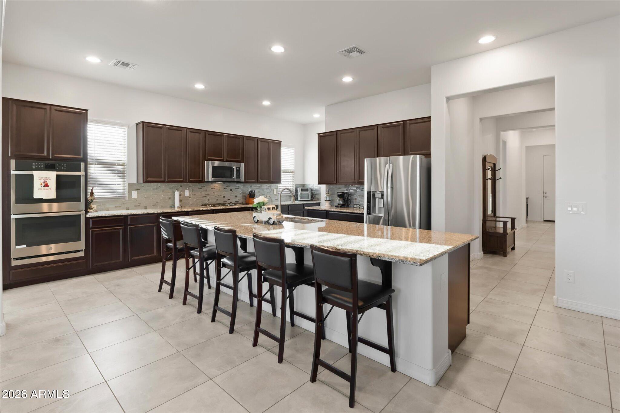 Kitchen with dark wood cabinets, stainless appliances, and a large granite island lined with bar stools.