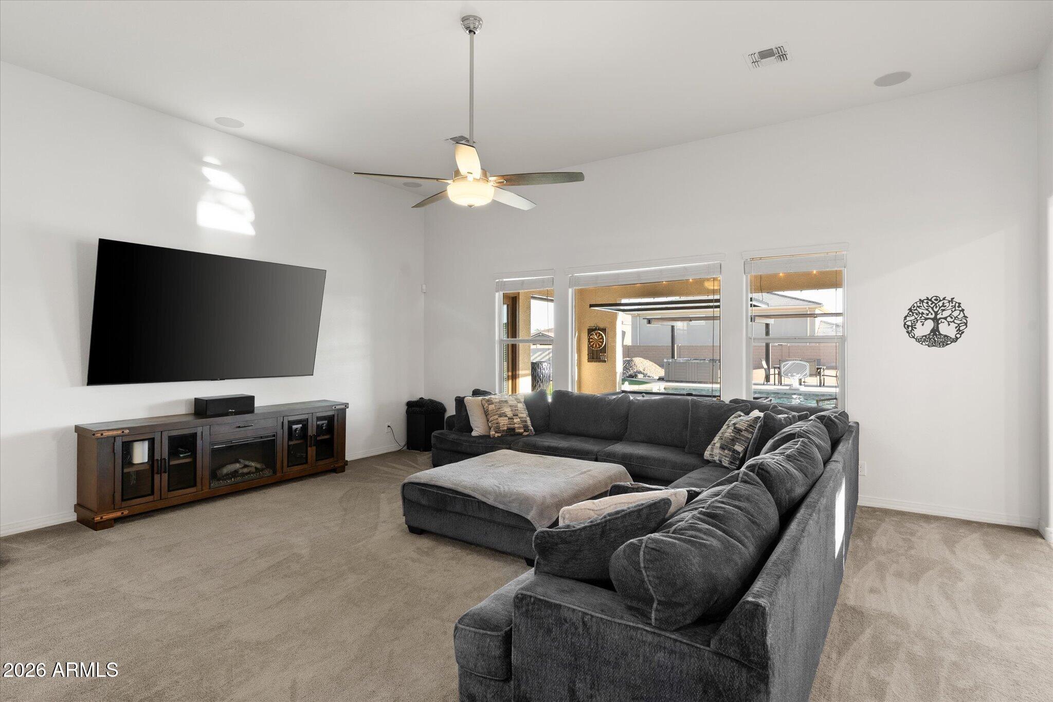 Living room with a charcoal sectional, wall-mounted TV, and windows overlooking a backyard pool.