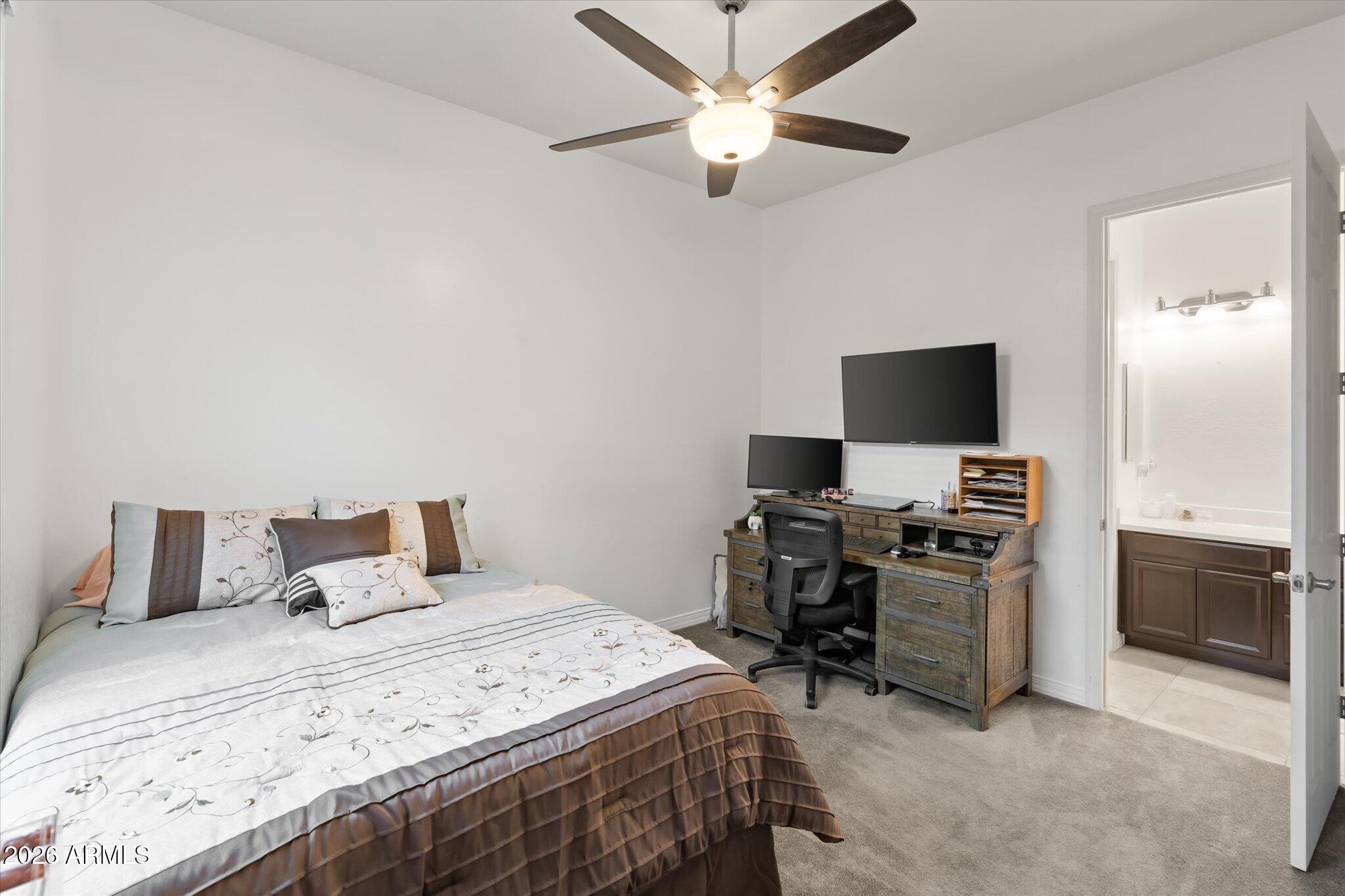 Furnished bedroom with a bed and desk beside an open doorway to an ensuite bathroom.