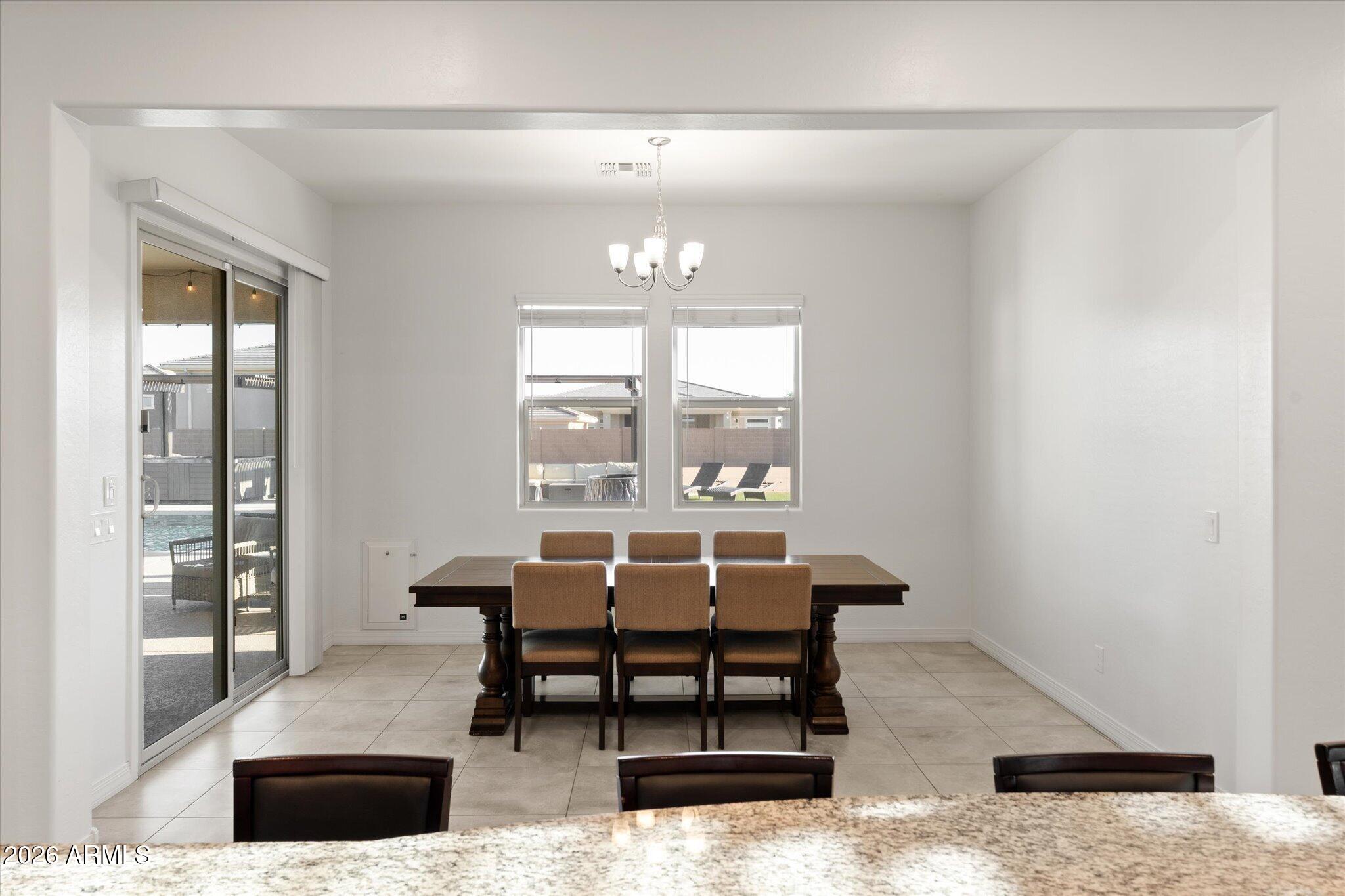 Dining room with a dark wood table, chandelier, and sliding glass door overlooking a pool.