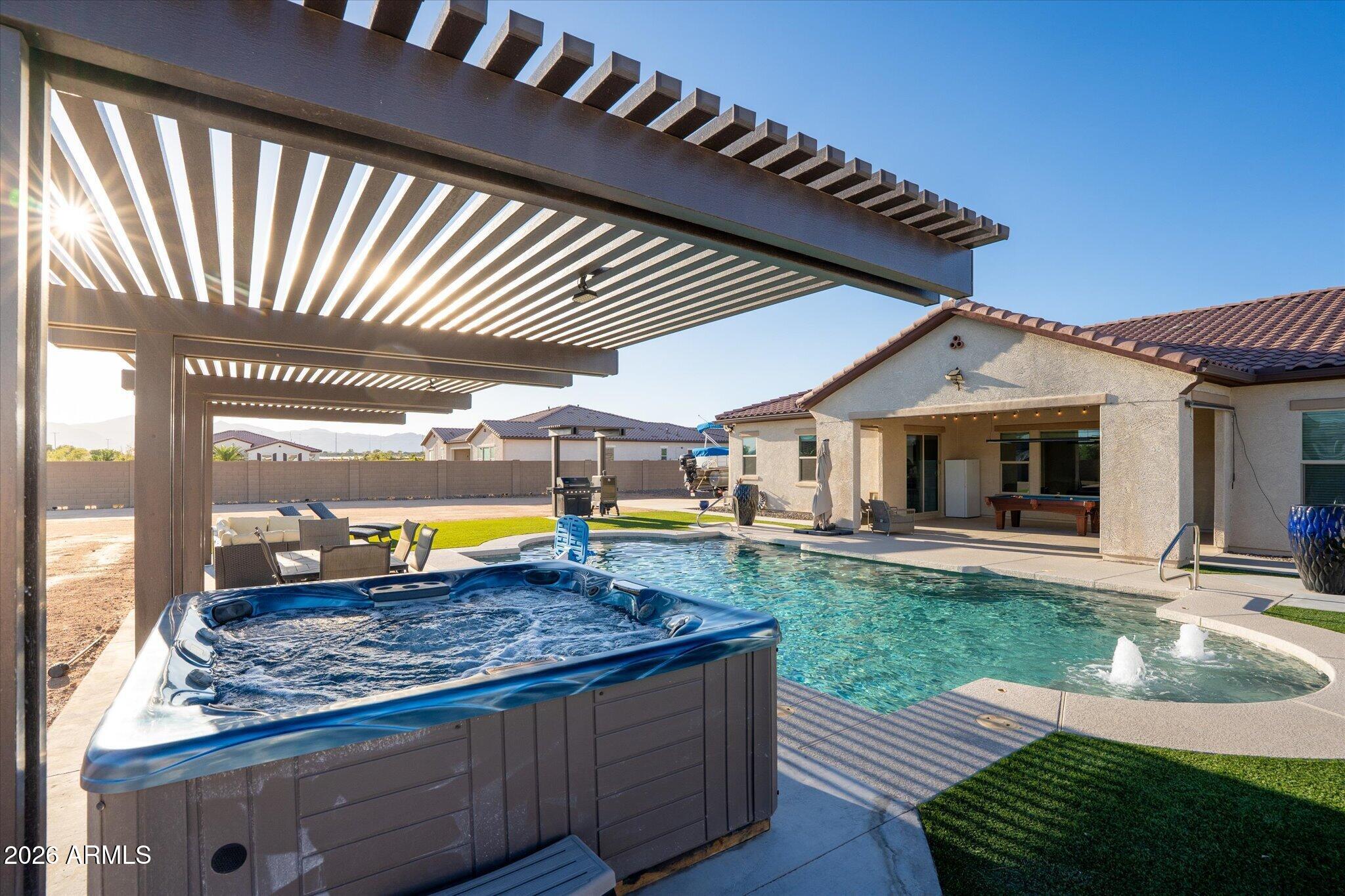 Backyard pool and raised hot tub beneath a large pergola, with patio seating and distant mountains.
