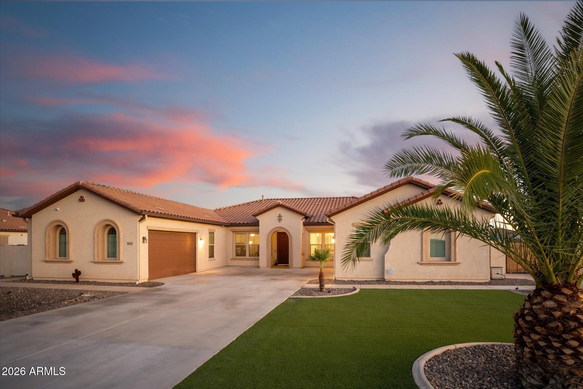 Single-story stucco home with arched windows, a tile roof, and palm trees at dusk.