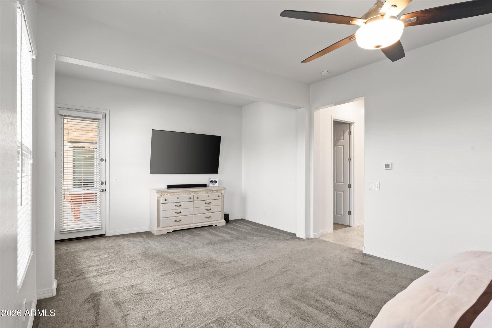 Bedroom with gray carpet, ceiling fan, wall-mounted television, and dresser.