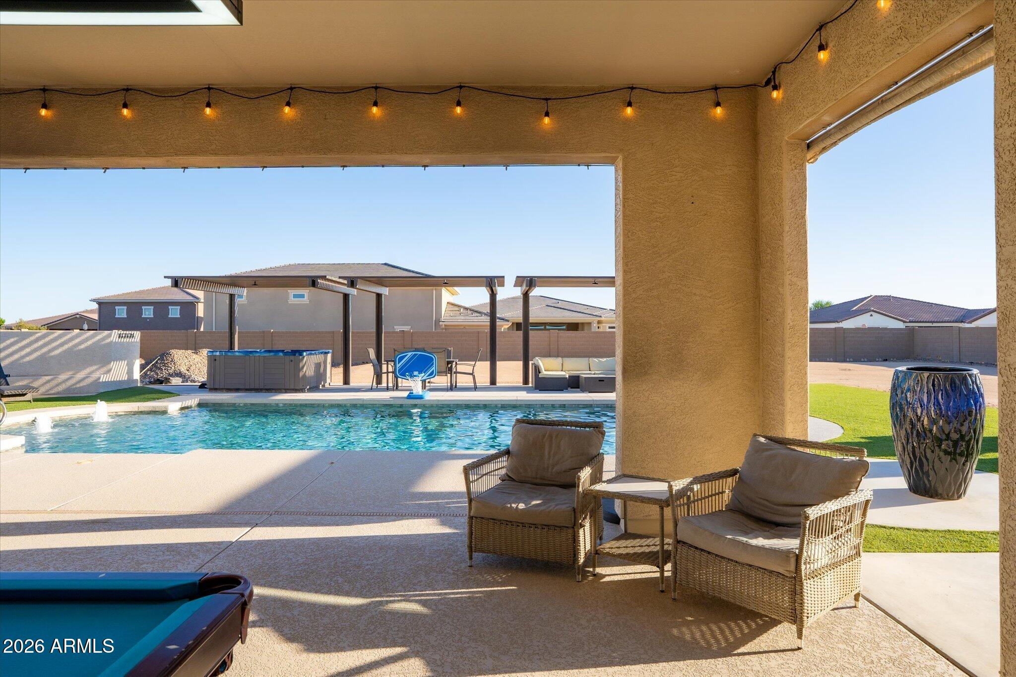 Backyard pool and covered patio with wicker seating, hot tub, and basketball hoop.
