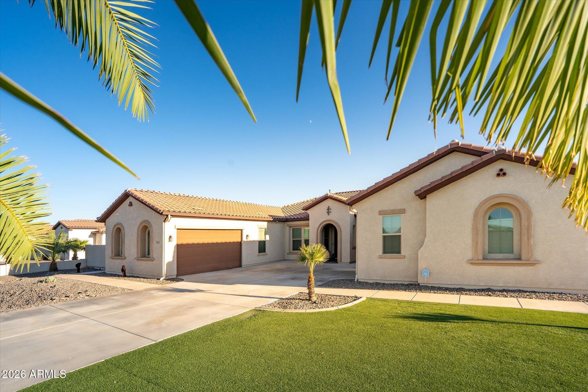 Stucco home with a tile roof, arched windows, two-car garage, palm trees, and a green lawn.