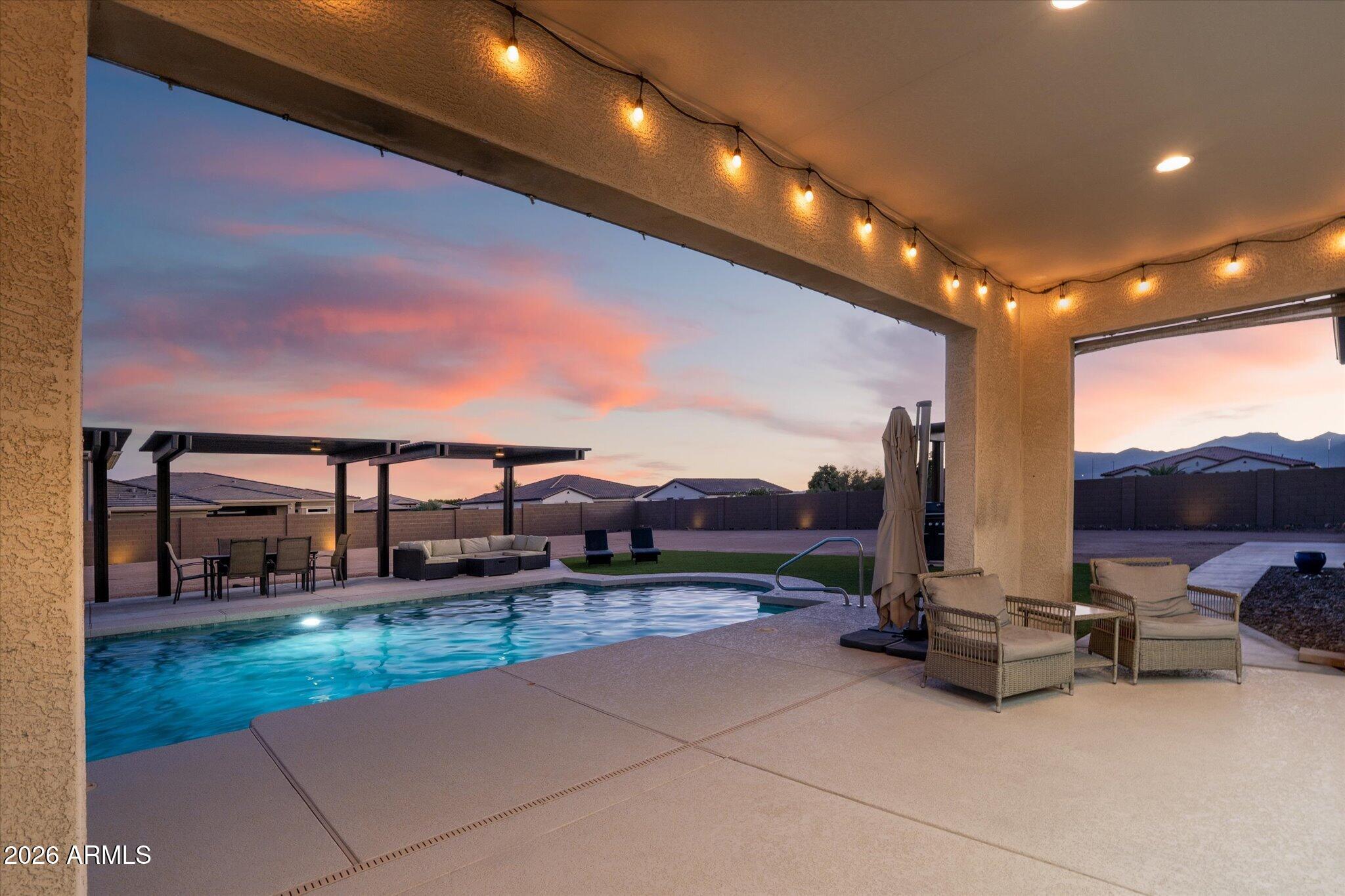 Backyard pool beside a covered patio with string lights and mountains in the distance.
