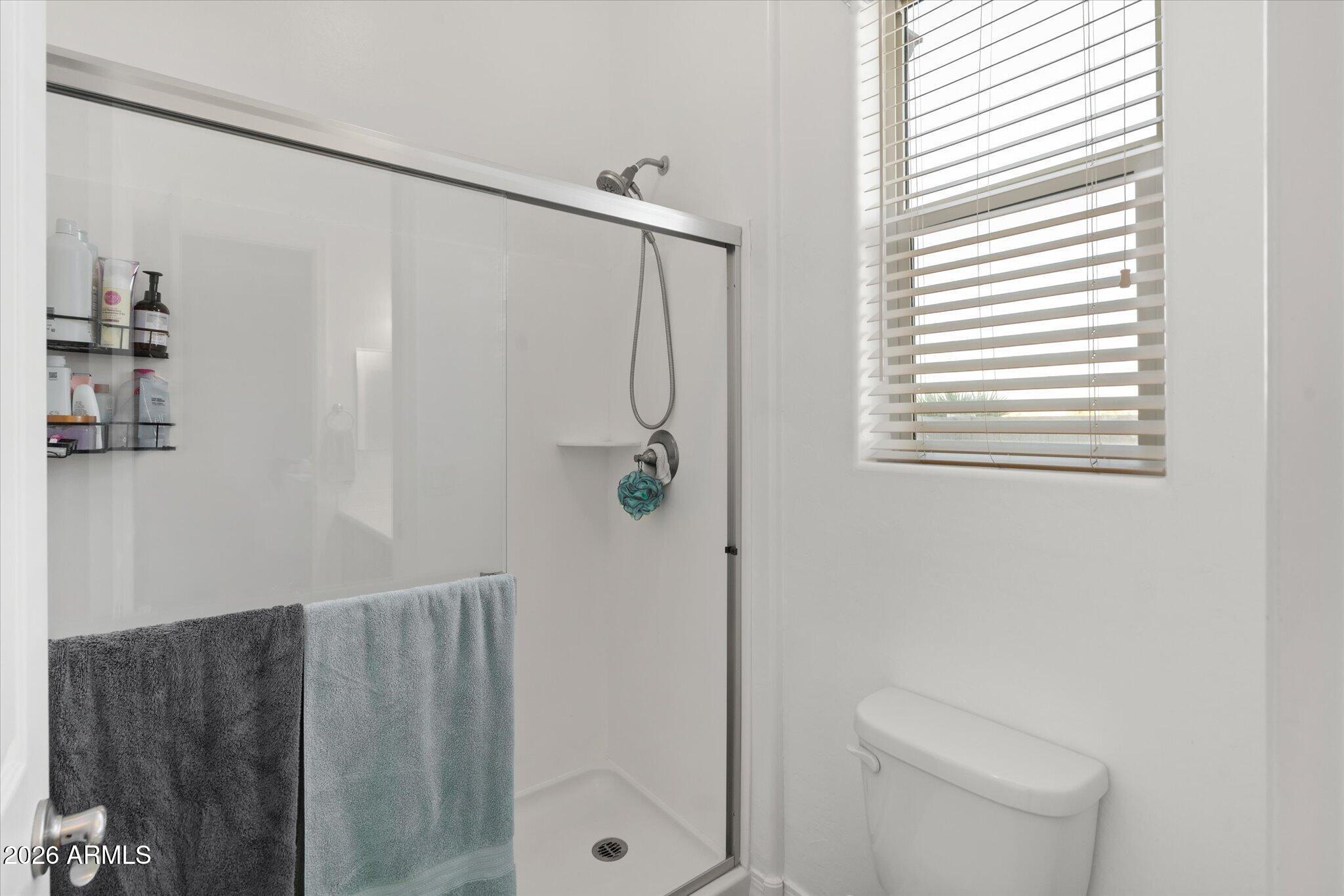 Bathroom with a glass-enclosed walk-in shower, window with blinds, and toilet.