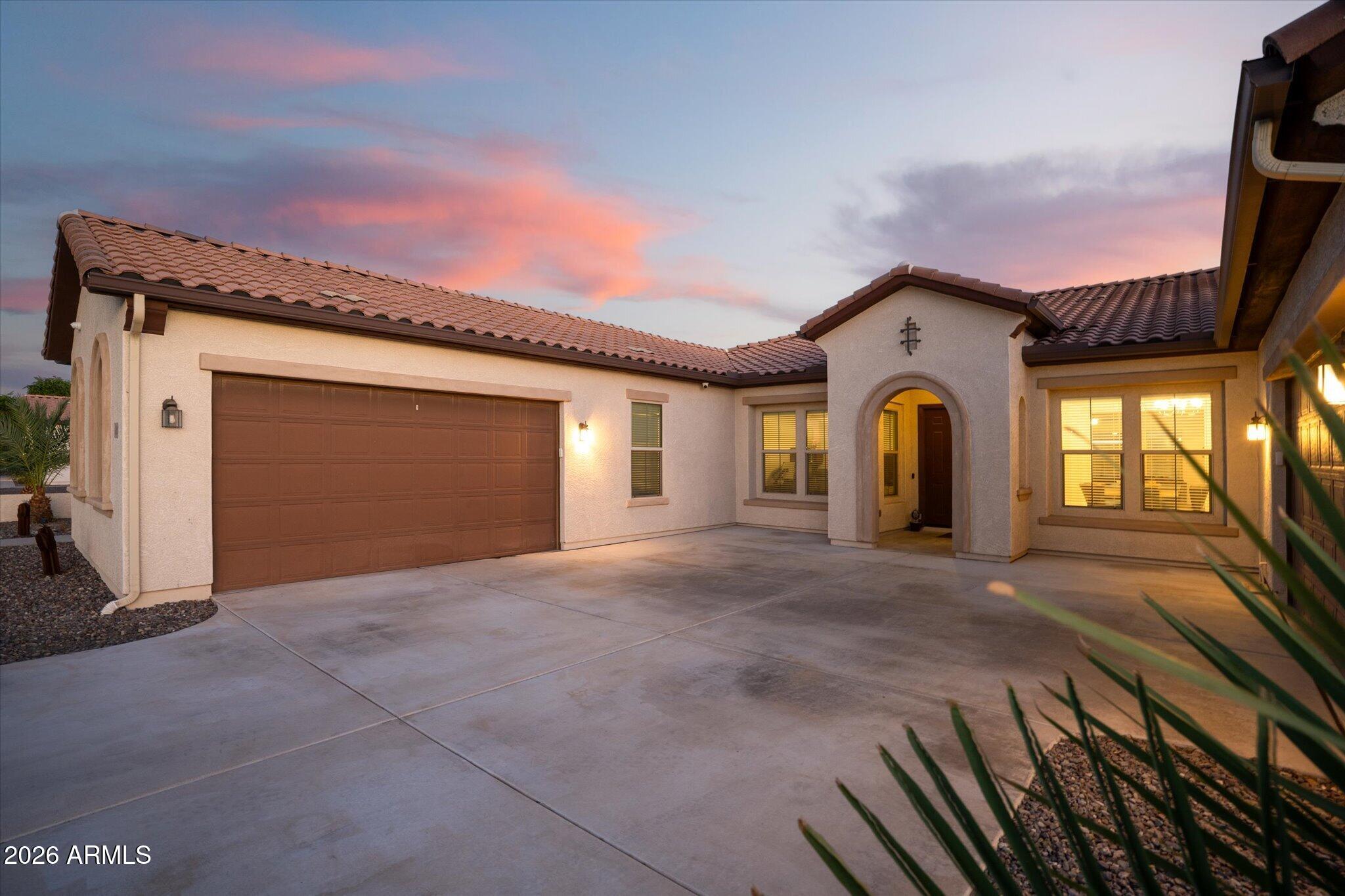 Single-story stucco home with a wide garage and arched entry at dusk.