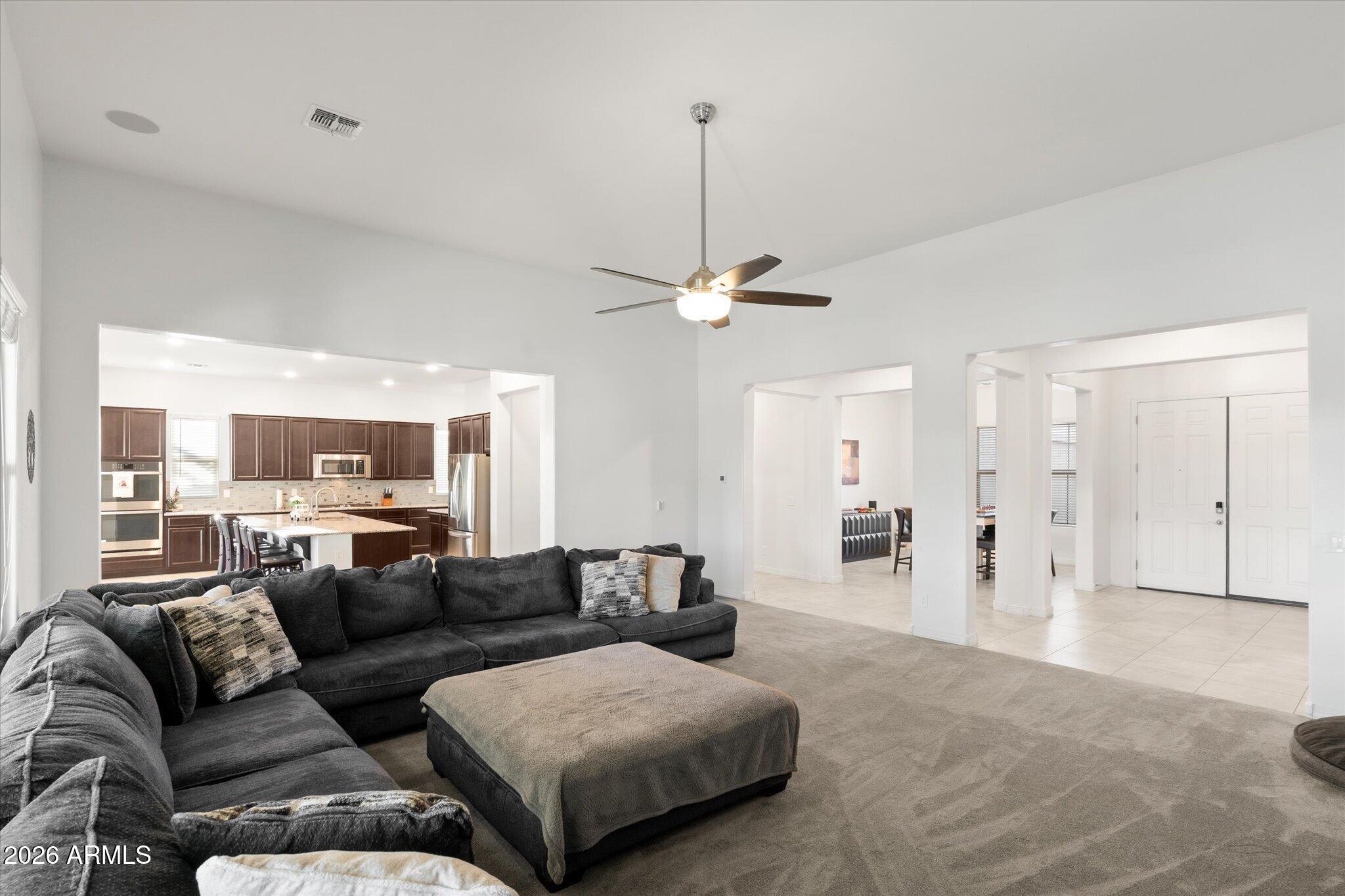Open-plan living room with a charcoal sectional and ottoman beside a kitchen with dark wood cabinets.