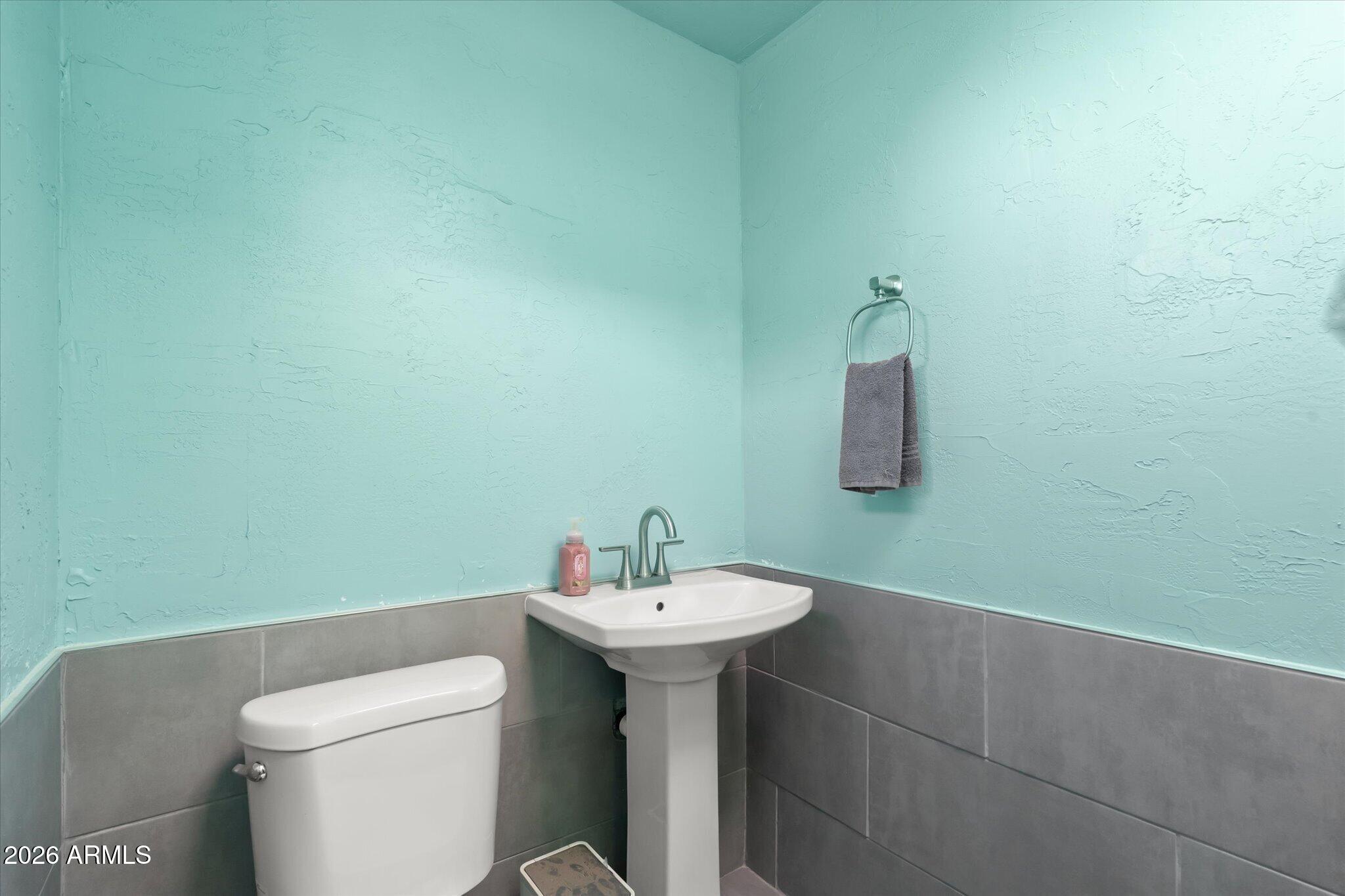 Bathroom with turquoise textured walls, gray tile wainscoting, a white toilet, and pedestal sink.