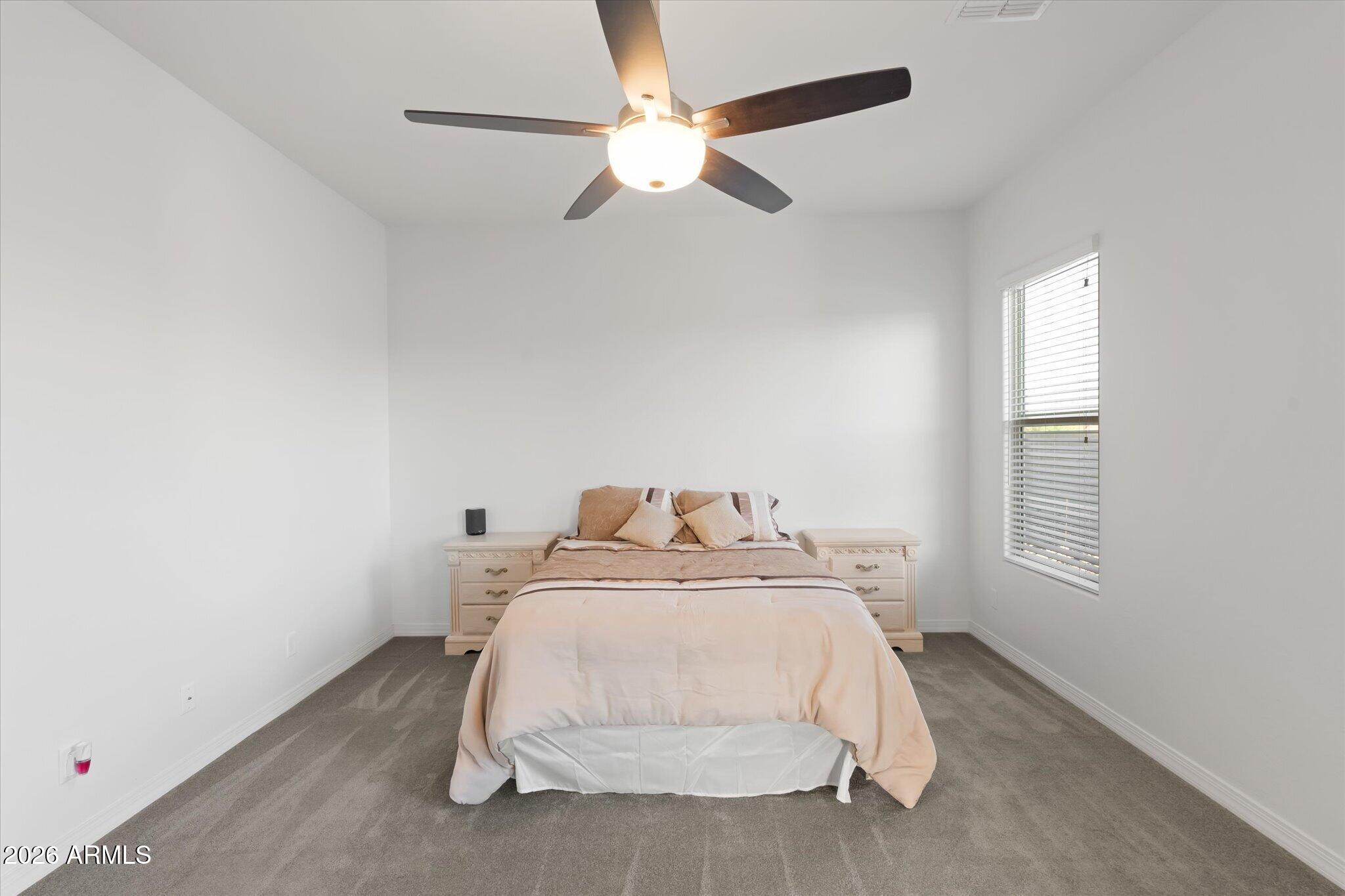 Bedroom with a centered bed, gray carpet, and ceiling fan.