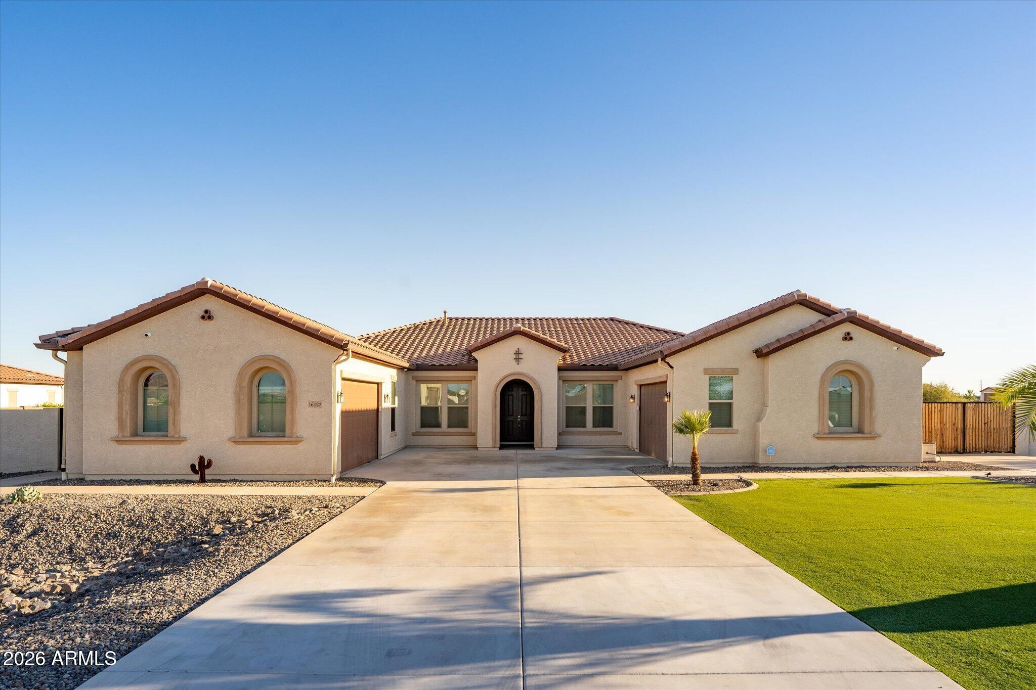 Single-story stucco home with a tiled roof, arched windows, and a broad concrete driveway.