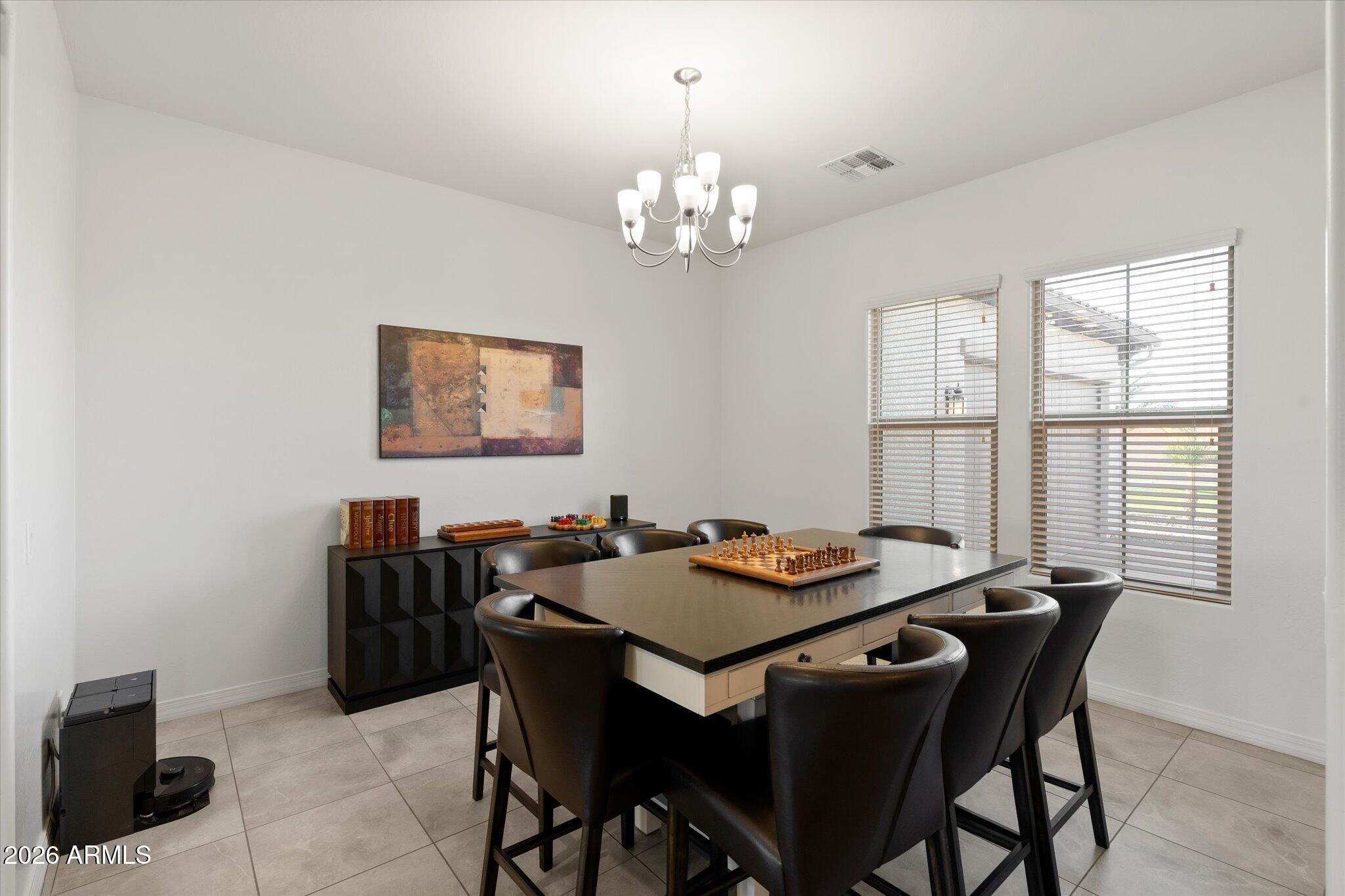 Furnished dining room with a chess set on the table and two bright windows with blinds.