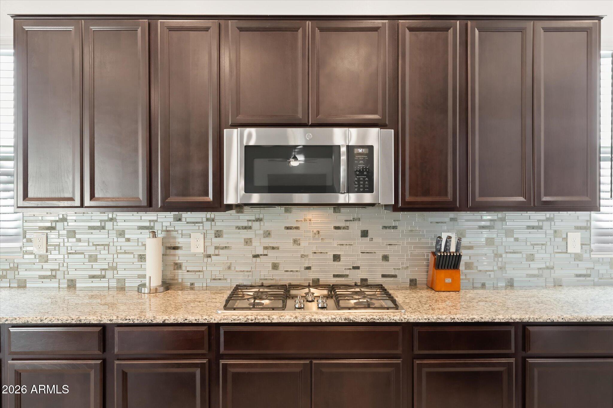 Kitchen with dark wood cabinets, a stainless steel microwave, gas cooktop, and mosaic tile backsplash.