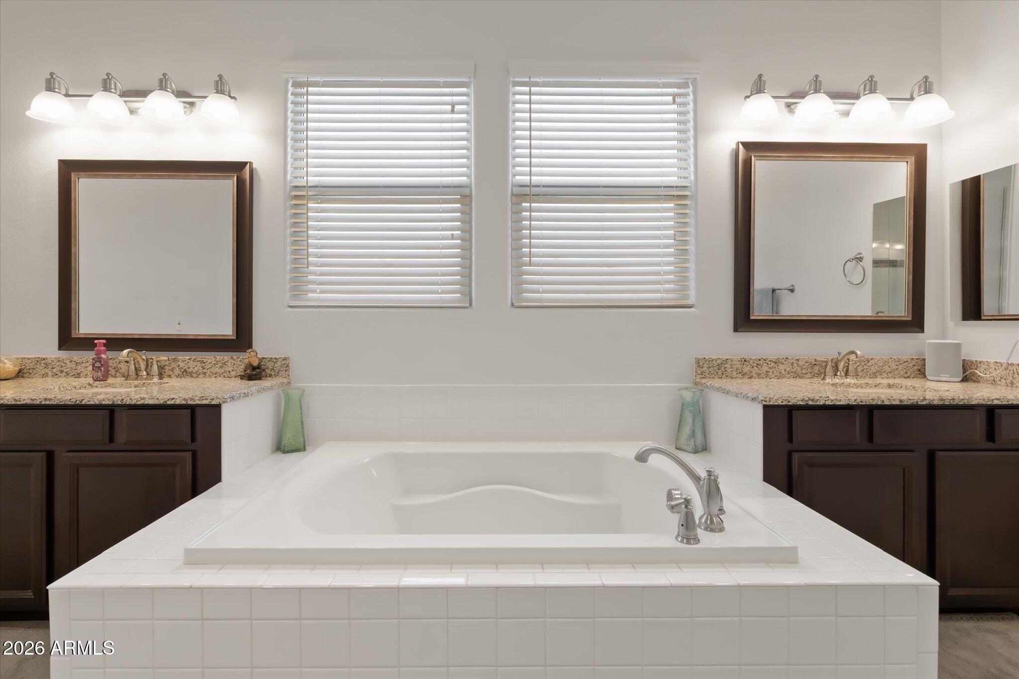 Bathroom with a large tiled soaking tub between dark wood vanities and windows.