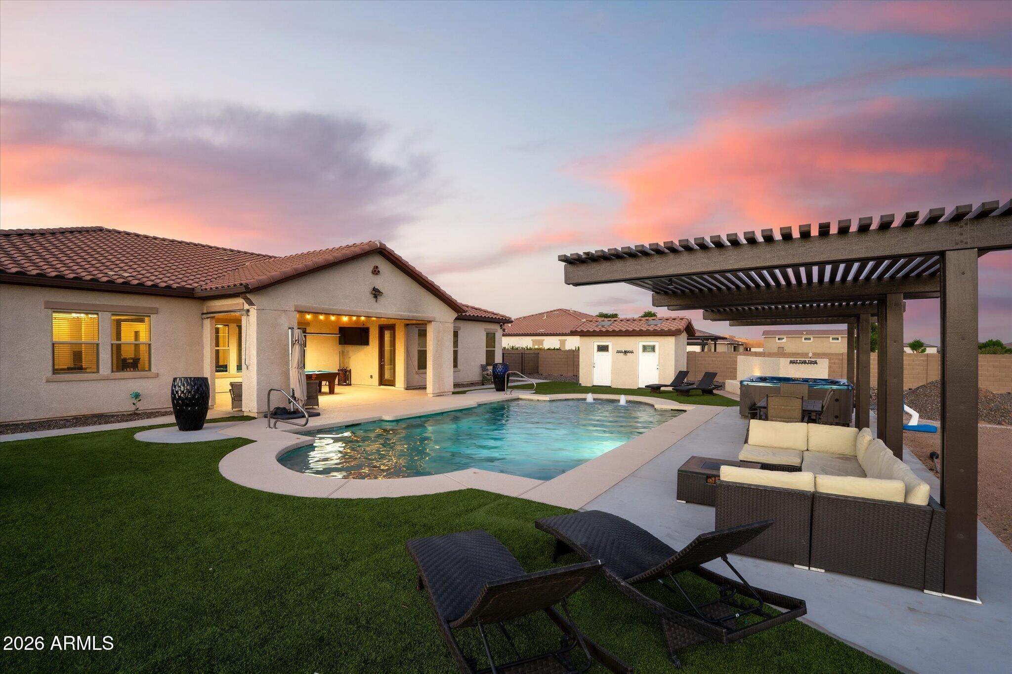 Backyard pool and covered patio with outdoor lounge seating beneath a colorful dusk sky.