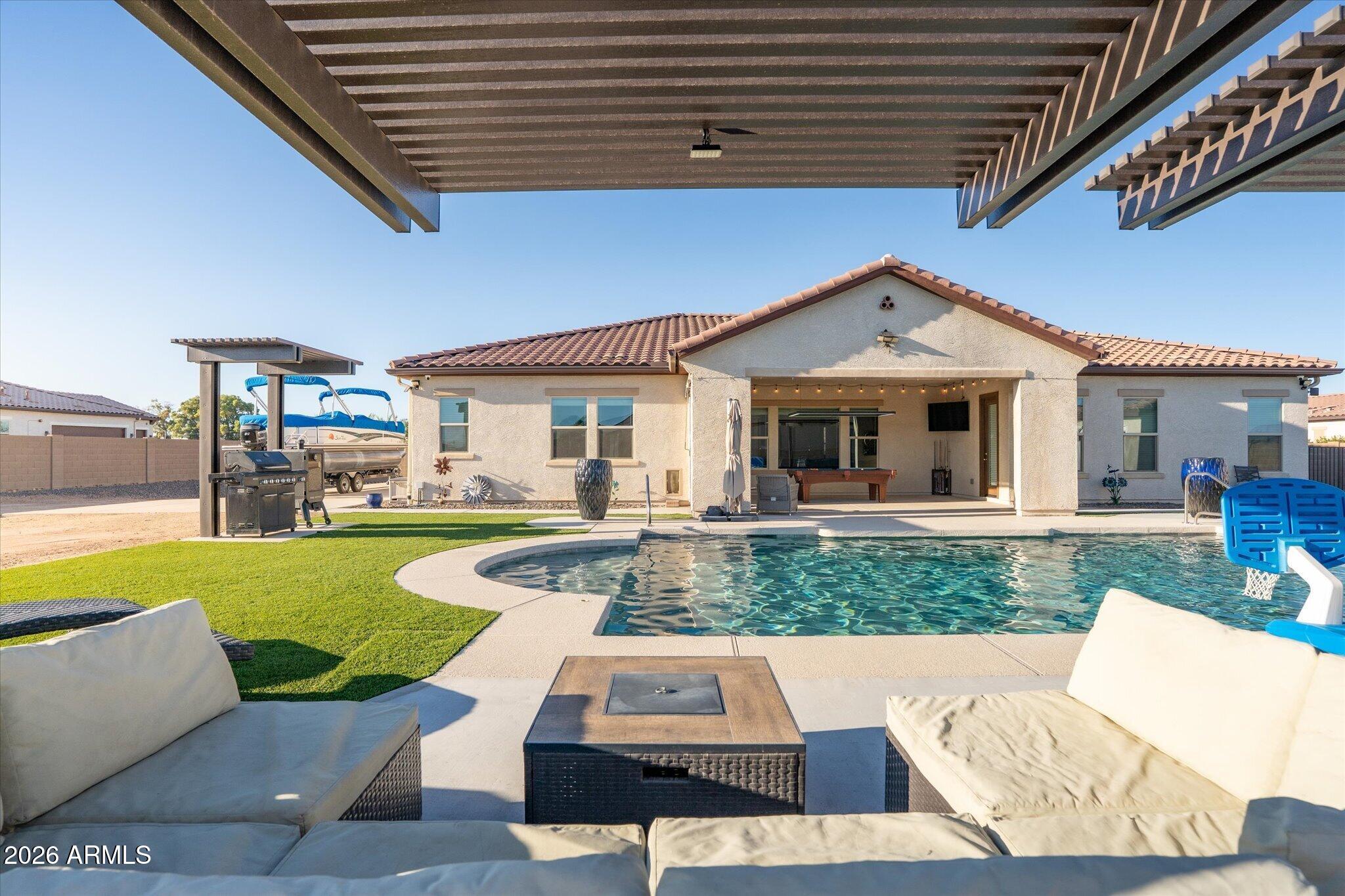 Home’s backyard with a swimming pool, covered patio, pergola, and outdoor seating.