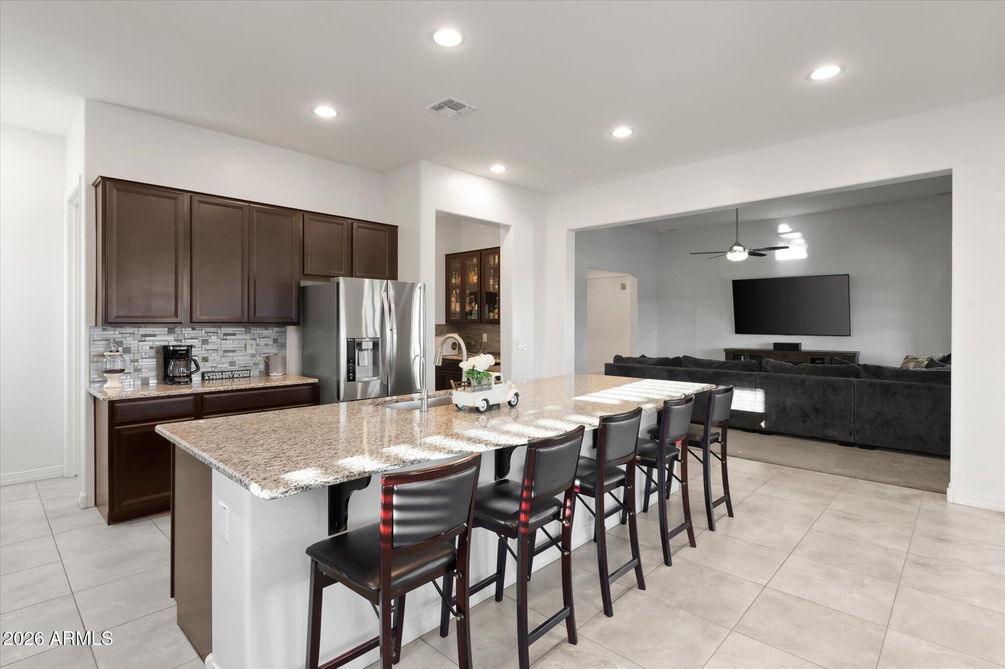 Open kitchen with a granite island and bar stools adjoining a living room with a large sectional.