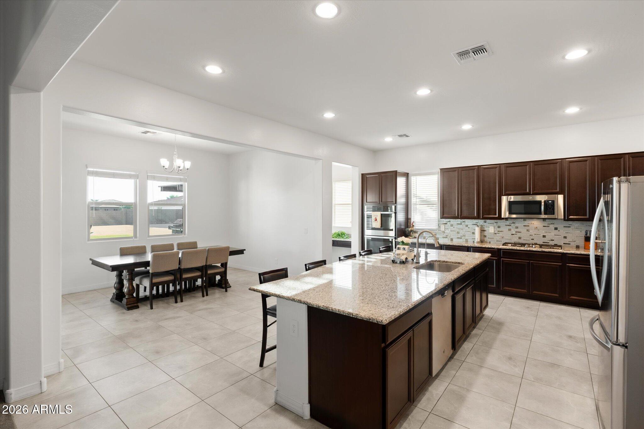 Open kitchen and dining area with a granite island, dark wood cabinets, and stainless steel appliances.