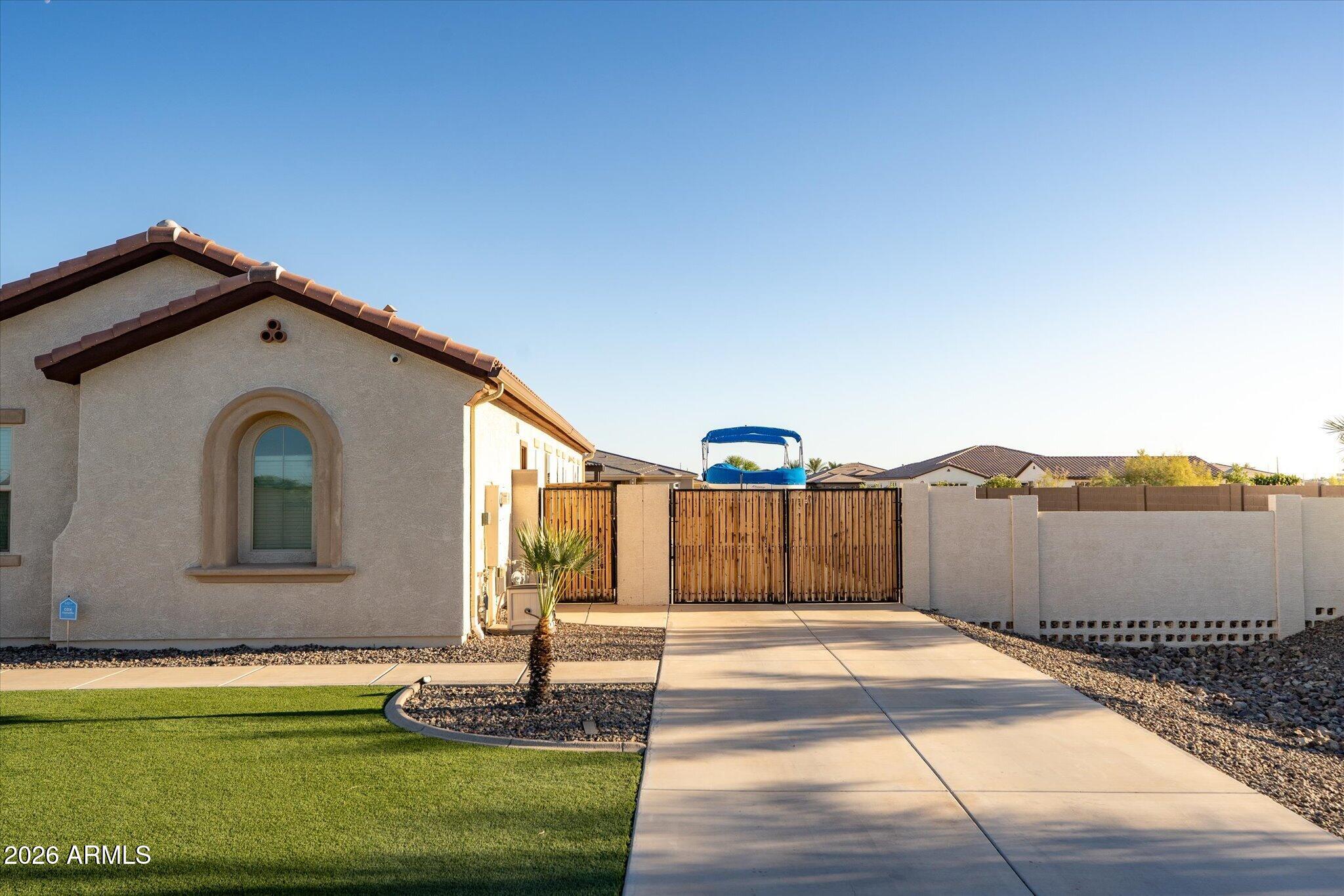 Home exterior with an arched window, artificial turf, and a driveway leading to a wooden gate.