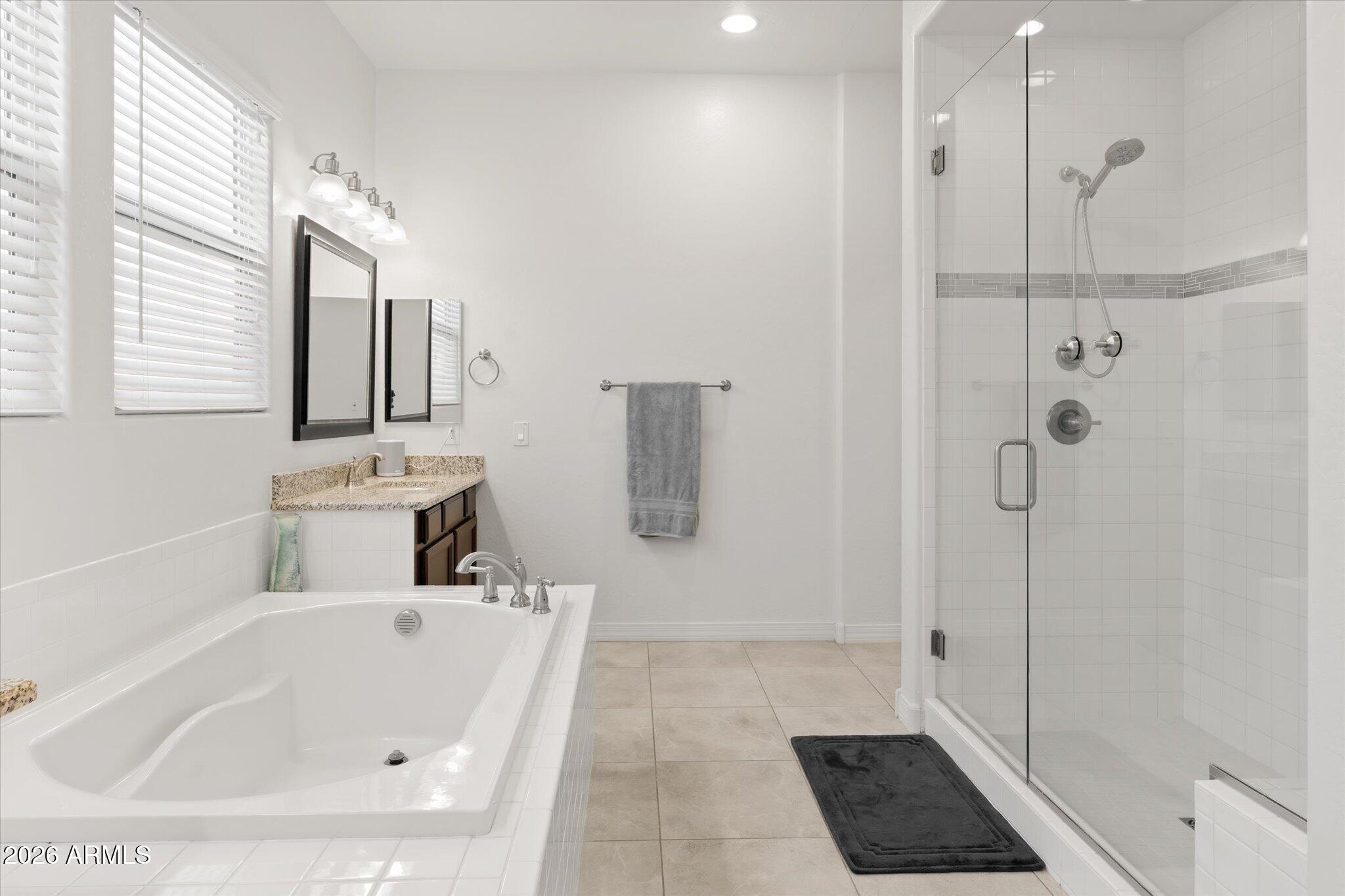Bathroom with a large soaking tub beside a glass-enclosed tiled shower and granite vanity.