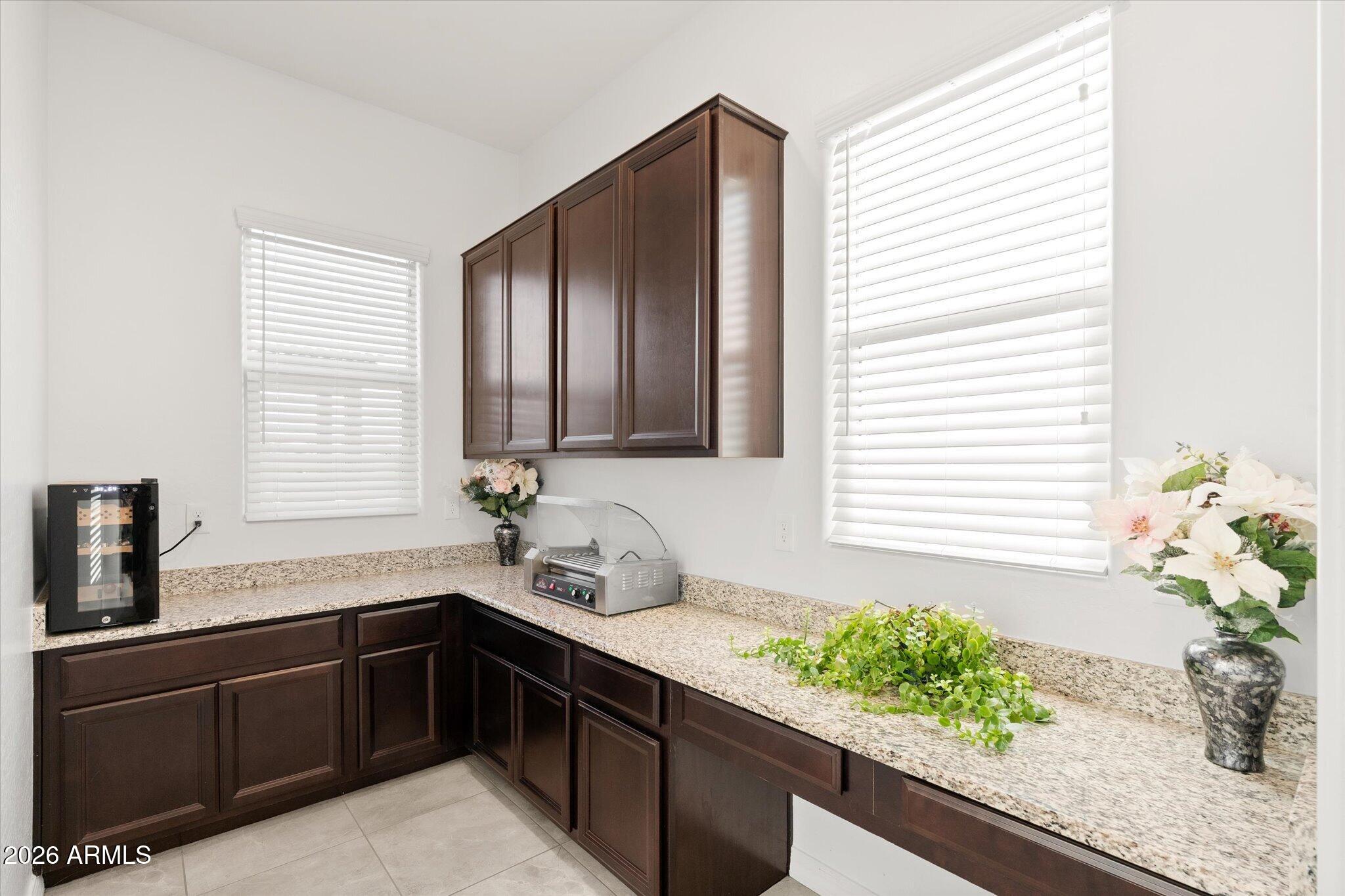 Kitchen workspace with dark wood cabinets, granite counters, bright windows, and decorative plants.