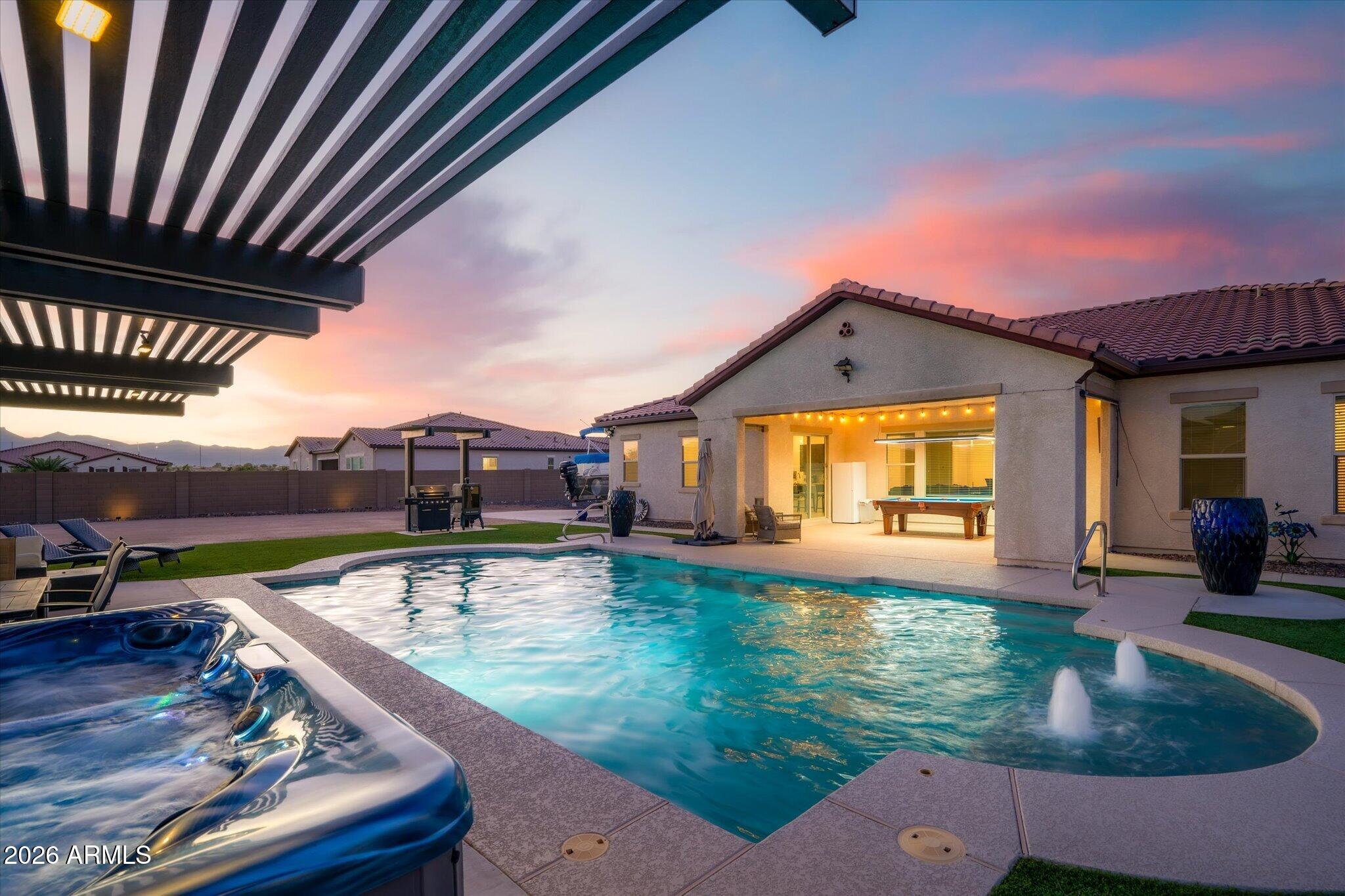 Backyard pool and spa beside an illuminated covered patio at sunset.
