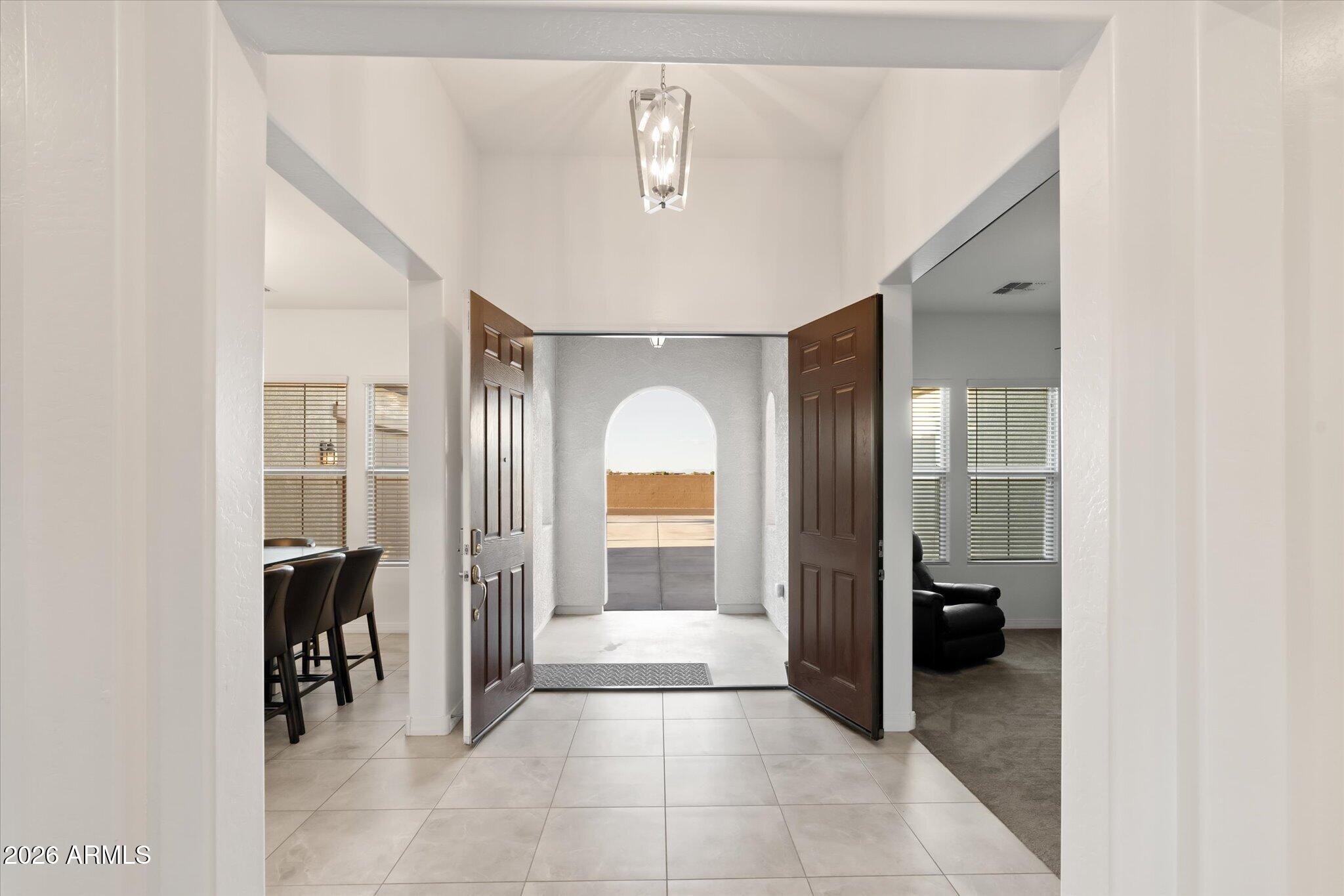 Entry foyer with open dark wood doors, tiled floors, and an arched opening to the patio.