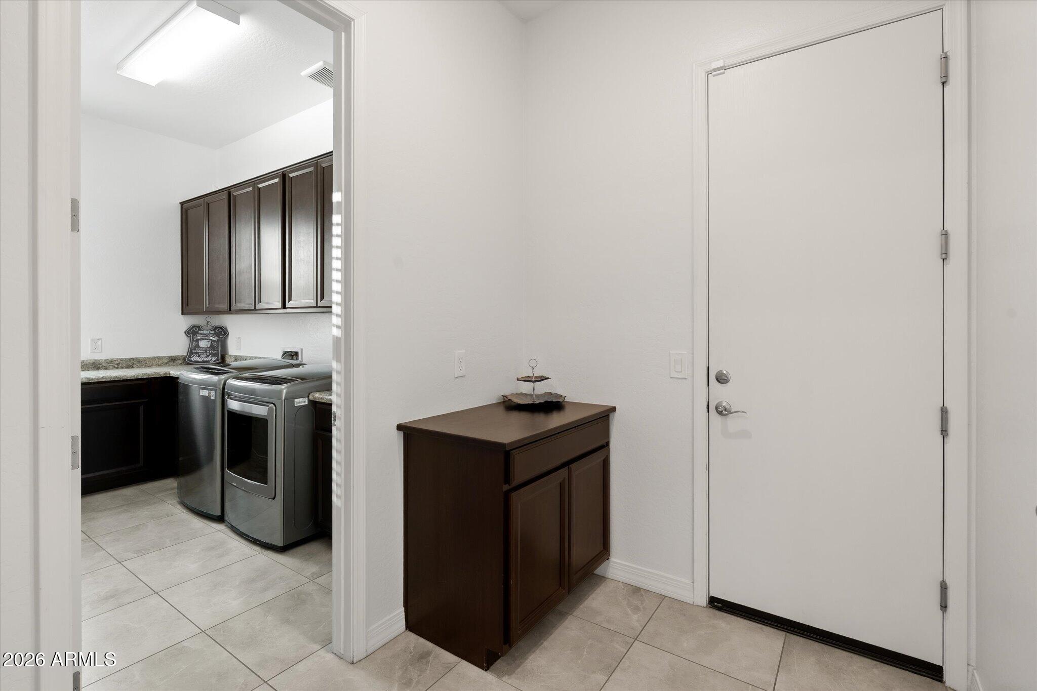 Tiled entryway with a dark wood cabinet beside the front door and an adjoining laundry room.