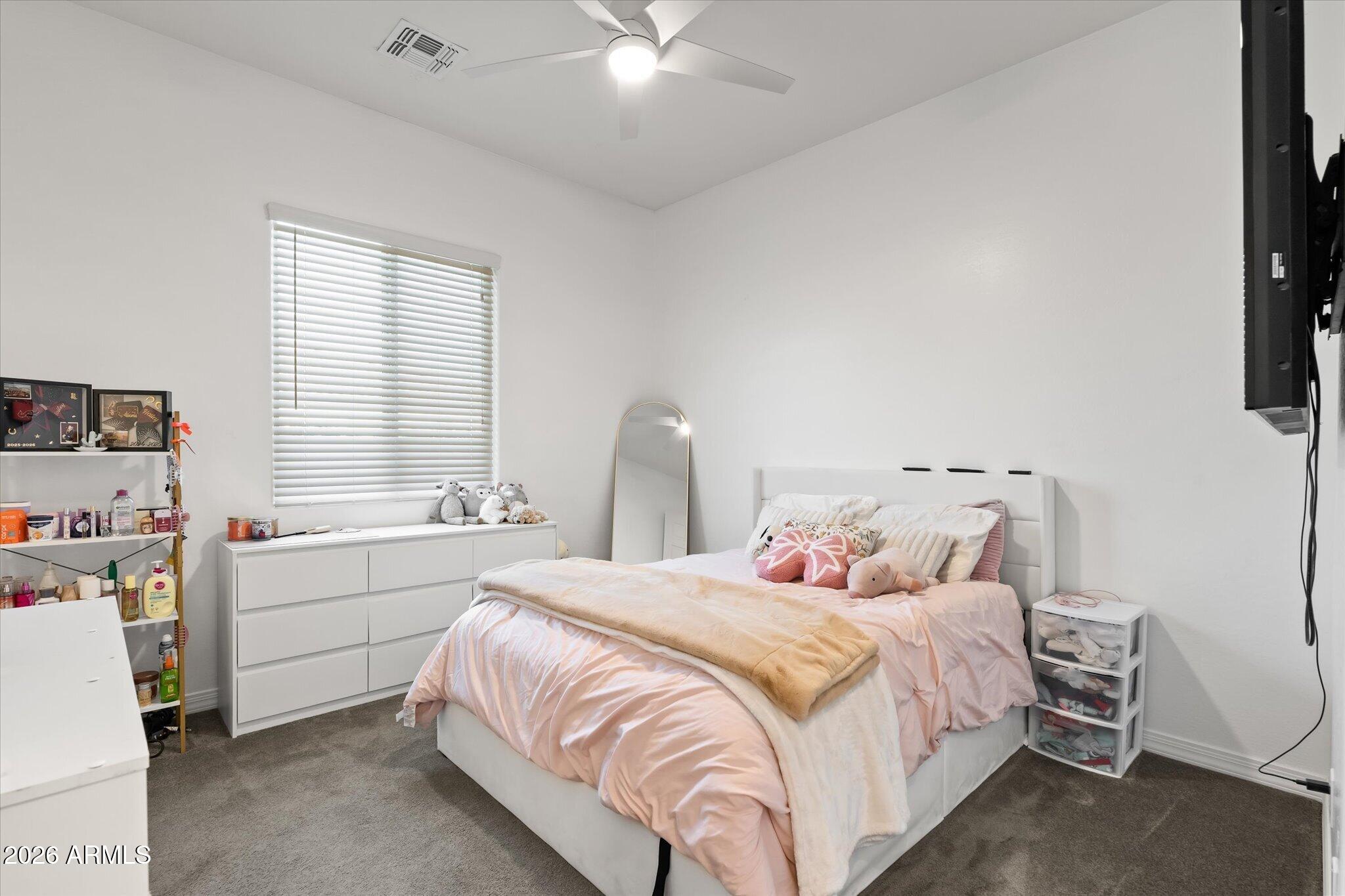 Bedroom with pale pink bedding, white dresser, window blinds, and a ceiling fan.