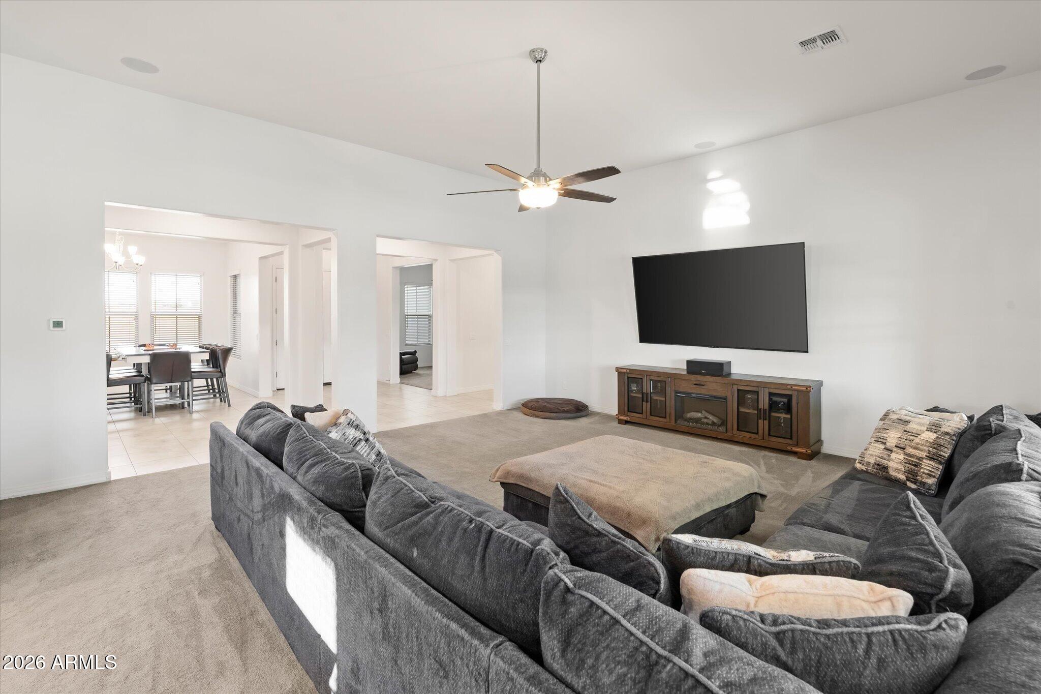 Furnished living room with a large gray sectional, ottoman, wall-mounted TV, and adjoining dining area.