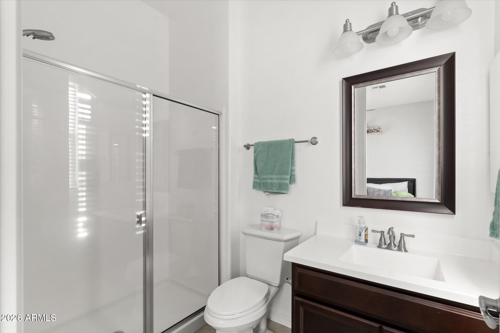Bathroom with glass shower, dark wood vanity, framed mirror, and teal hand towel