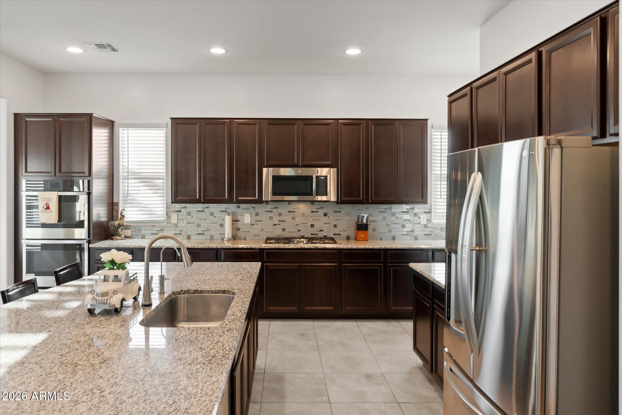 Kitchen with dark wood cabinets, granite island, stainless steel appliances, and a glass mosaic backsplash.