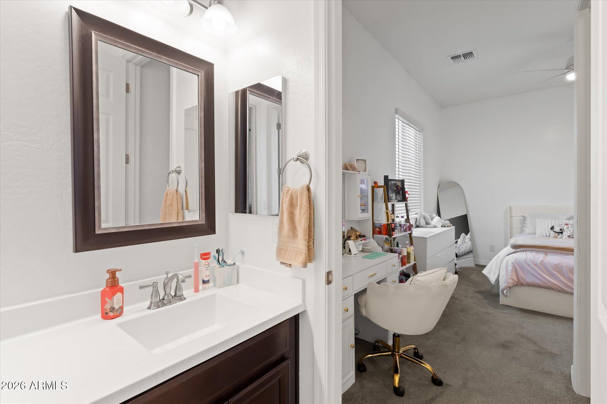 Bathroom vanity with dark wood cabinets and peach towels, opening onto a furnished bedroom.