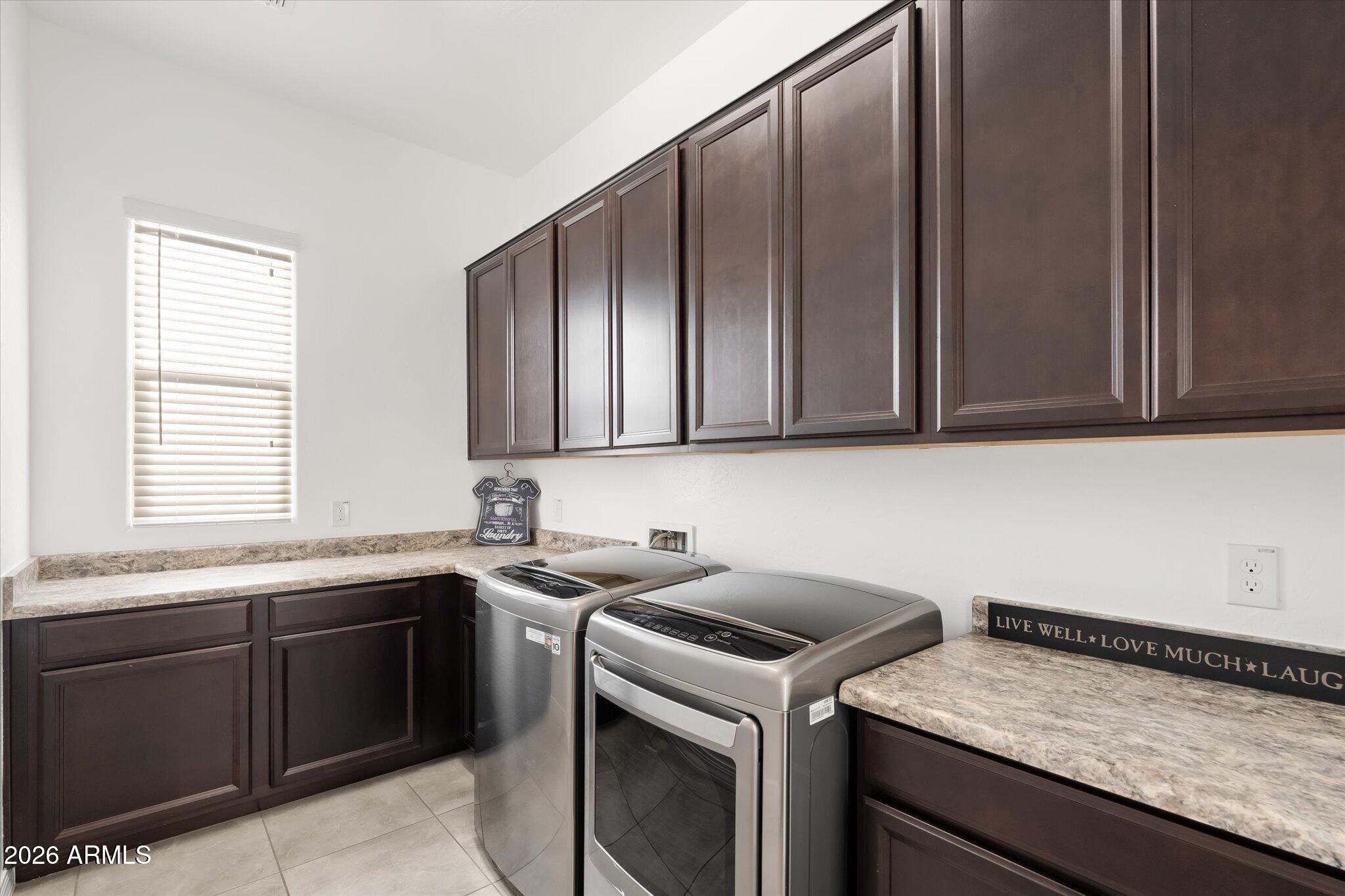 Laundry room with dark cabinets, stone-look counters, and a washer and dryer.