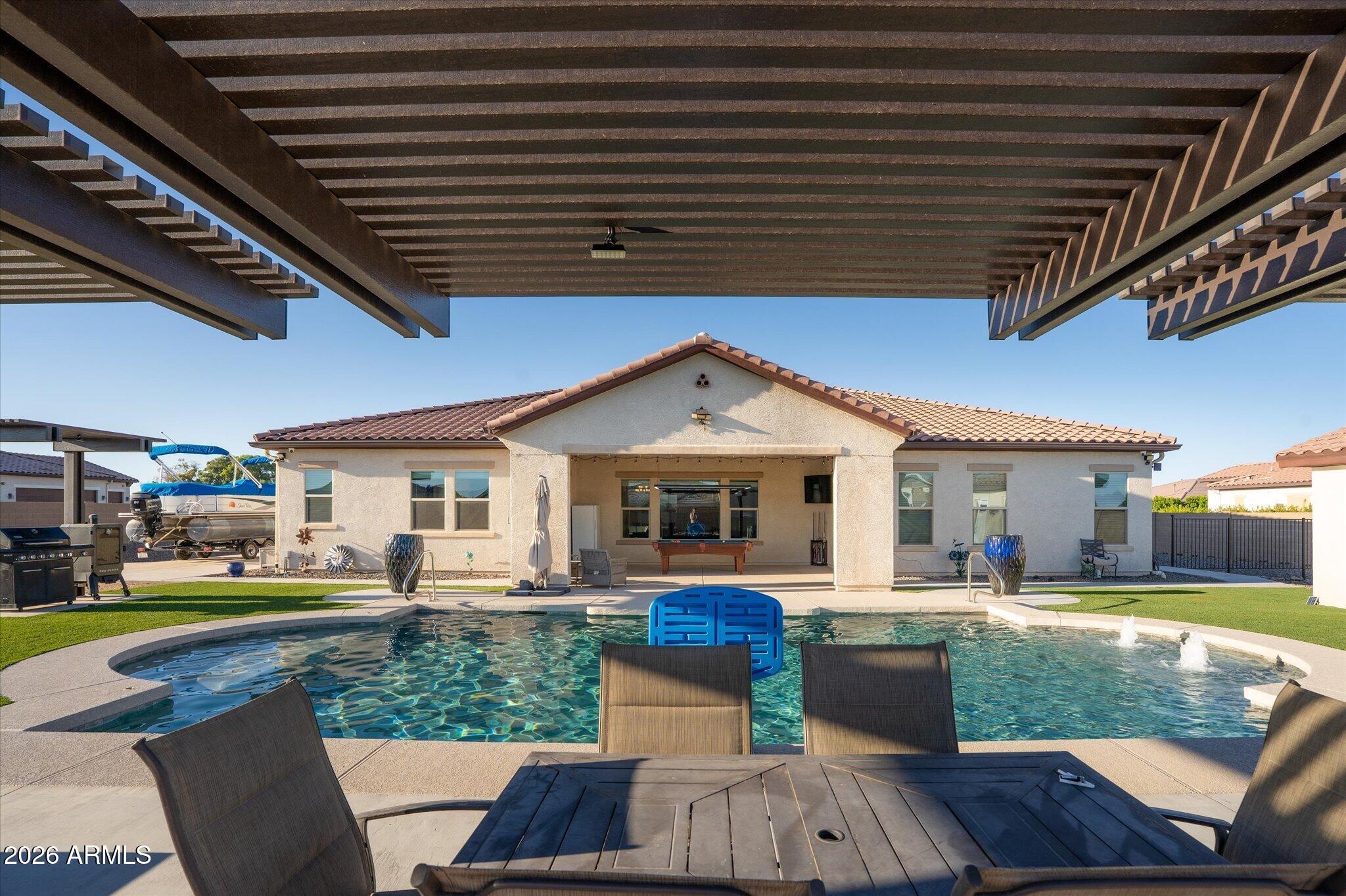 Backyard pool and covered patio behind a single-story stucco home, with a pergola and poolside seating.
