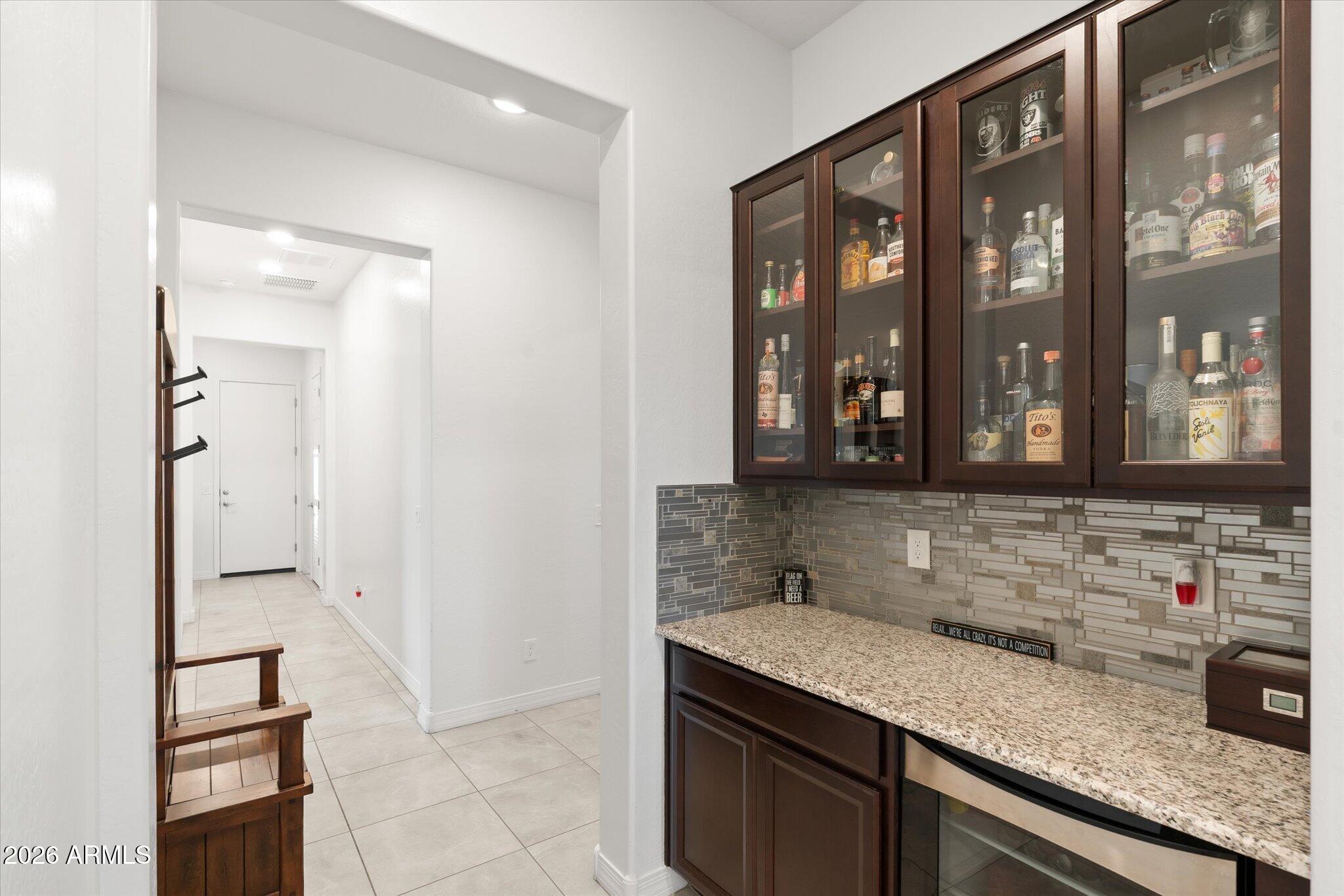 Wet bar with glass-front liquor cabinets, granite counter, mosaic backsplash, and beverage refrigerator.