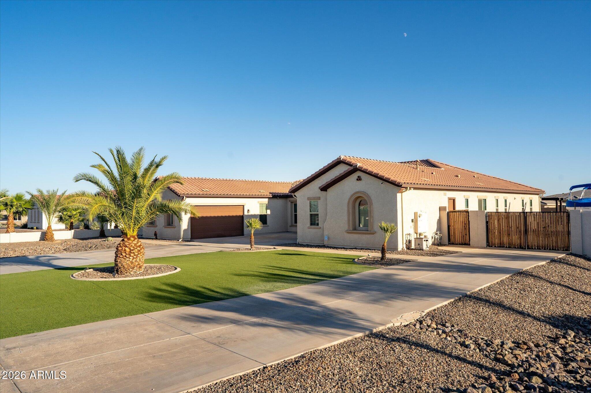 Single-story stucco home with a tile roof, palm trees, green lawn, and wide concrete driveway.