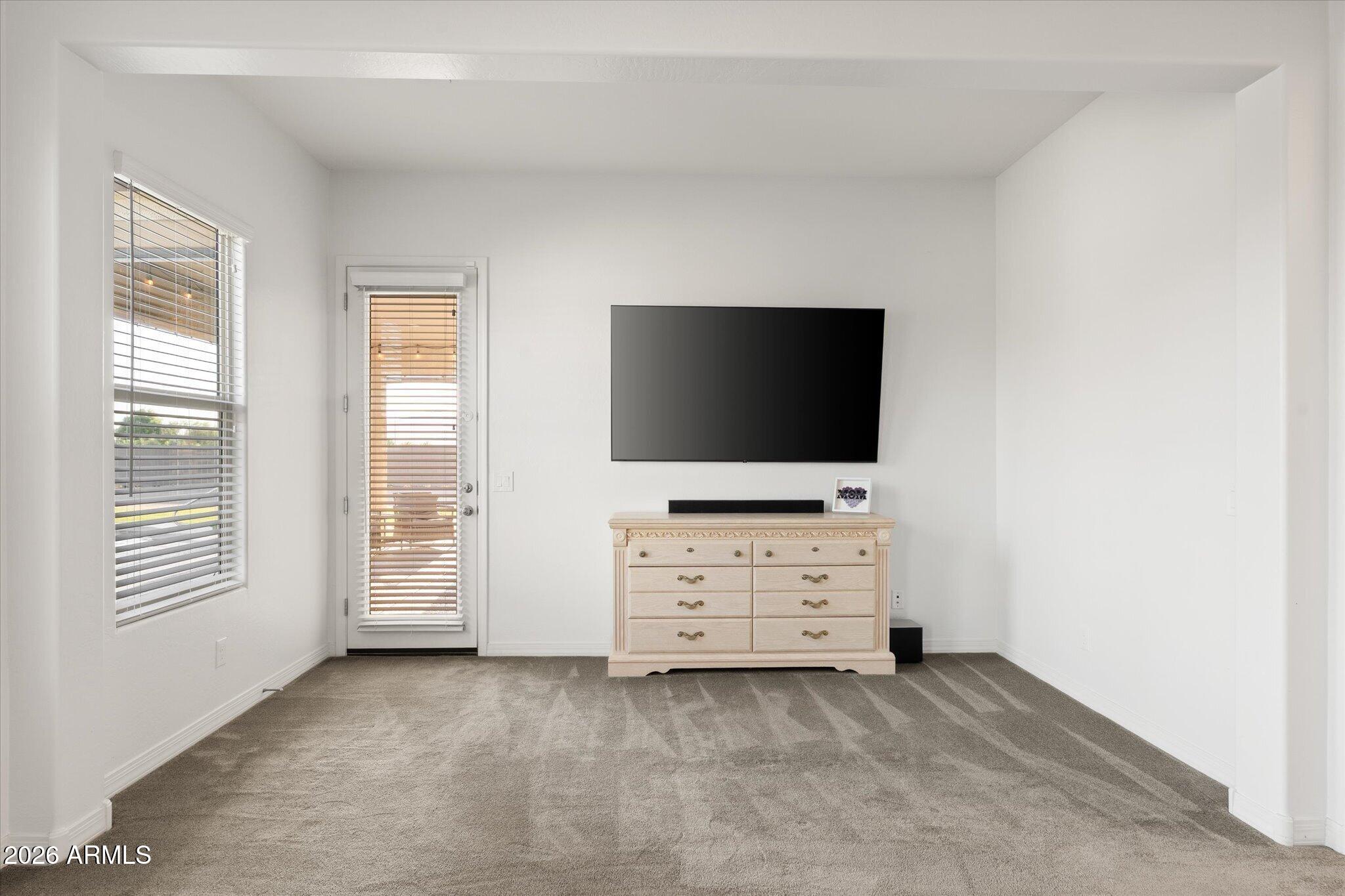 Carpeted room with a wall-mounted television, light dresser, and windows with blinds.