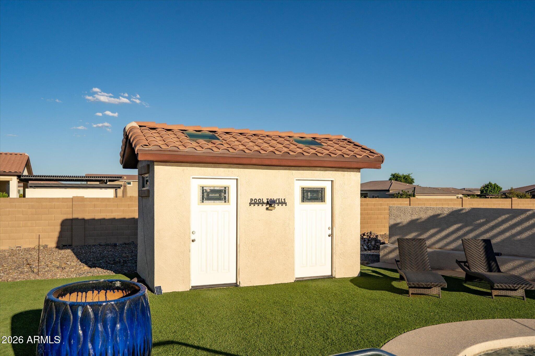 Backyard pool cabana with a terracotta tile roof, artificial turf, and woven lounge chairs.